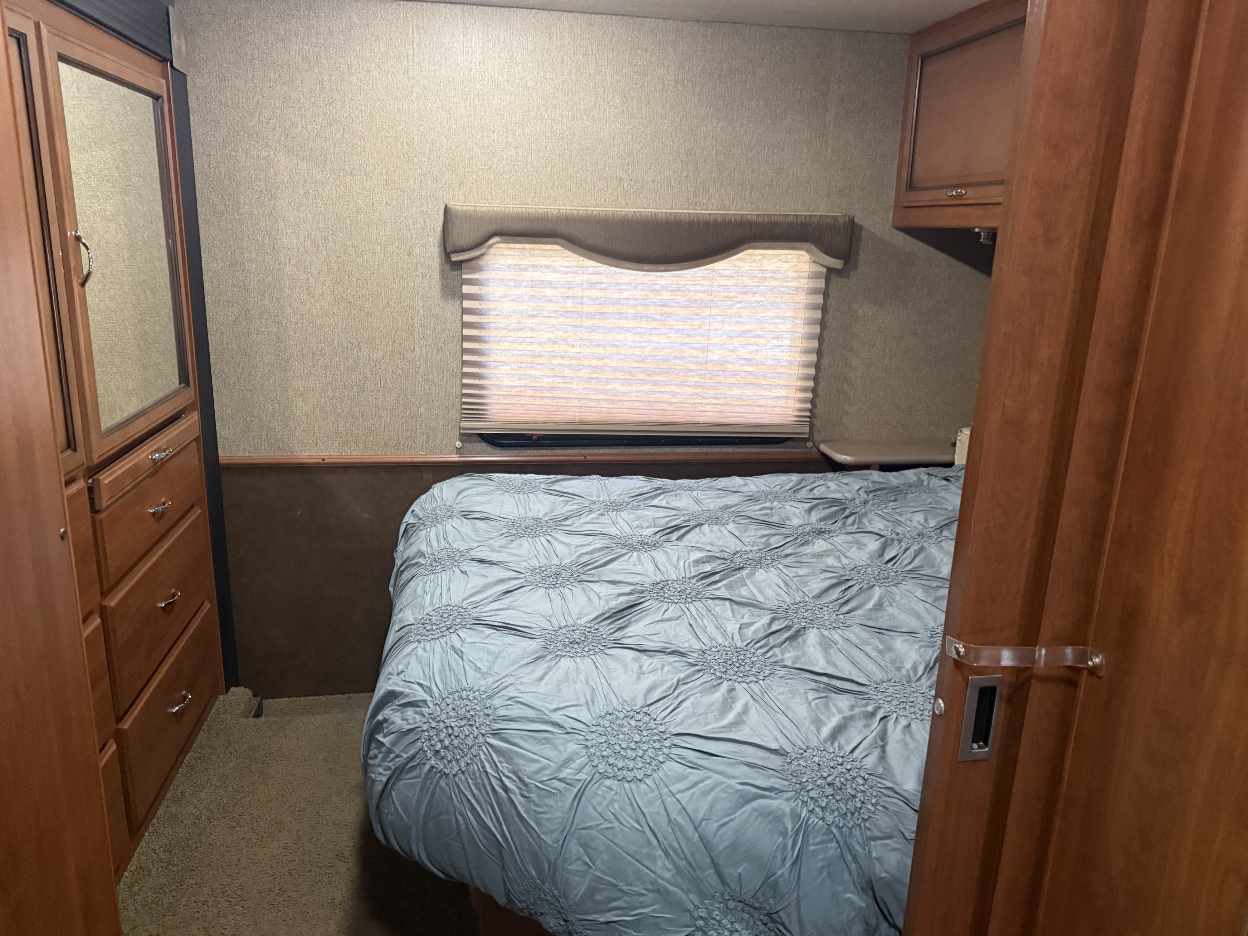 RV rental bedroom features a cozy bed with textured comforter, mirrored wardrobe, window with blinds, and built-in storage.. Tioga Ranger 2015