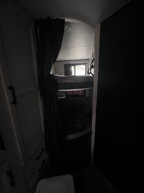 Inside an rv rental, showing dimly lit bunk beds. Curtains and a small window are visible from a dark entryway.. Jayco Jay Flight 2023