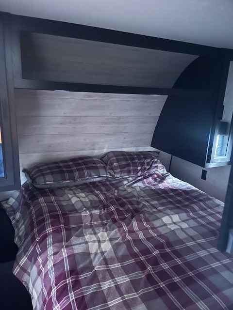 Interior view of an RV rental bedroom featuring a bed with purple plaid bedding, ideal for comfortable travel.. Jayco Jay Flight 2023