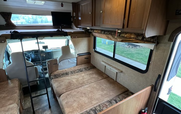 Cozy rv rental interior with bed, overhead bunk, driver's cabin, and windows. Perfect for travel adventures.. Coachmen Leprechaun 260QB 2016