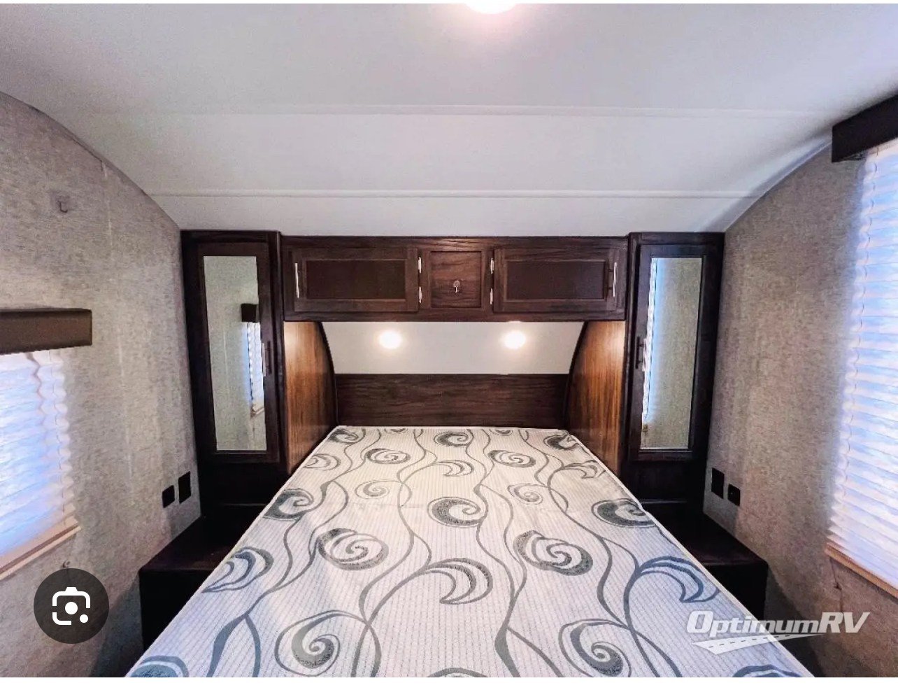 RV rental bedroom featuring a patterned bed, dark wood overhead cabinets, mirrored wardrobes, and warm accent lighting.. Forest River Cherokee 2019