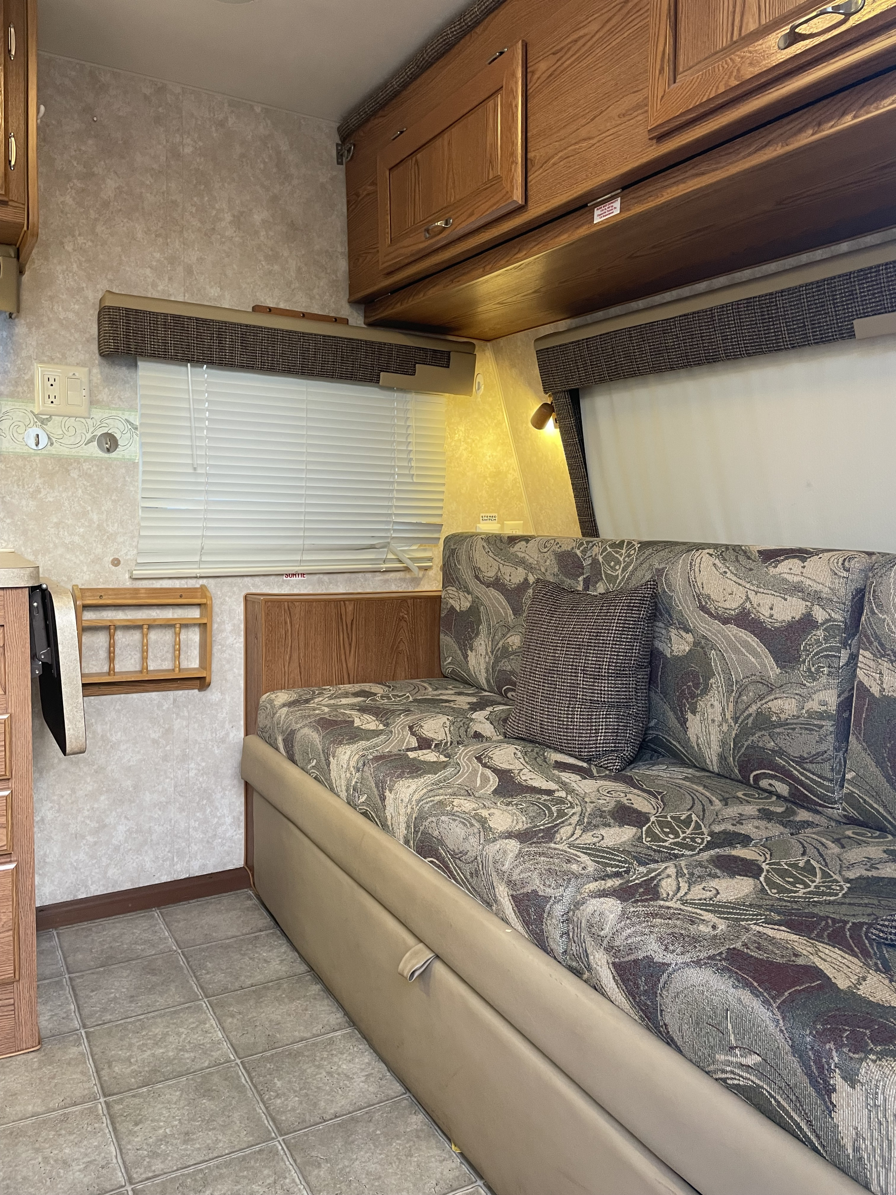 This RV rental interior shows a patterned sofa, wood cabinets, window with blinds, and tiled floor, offering a comfortable travel space.. Nash Nash Trailer 2008
