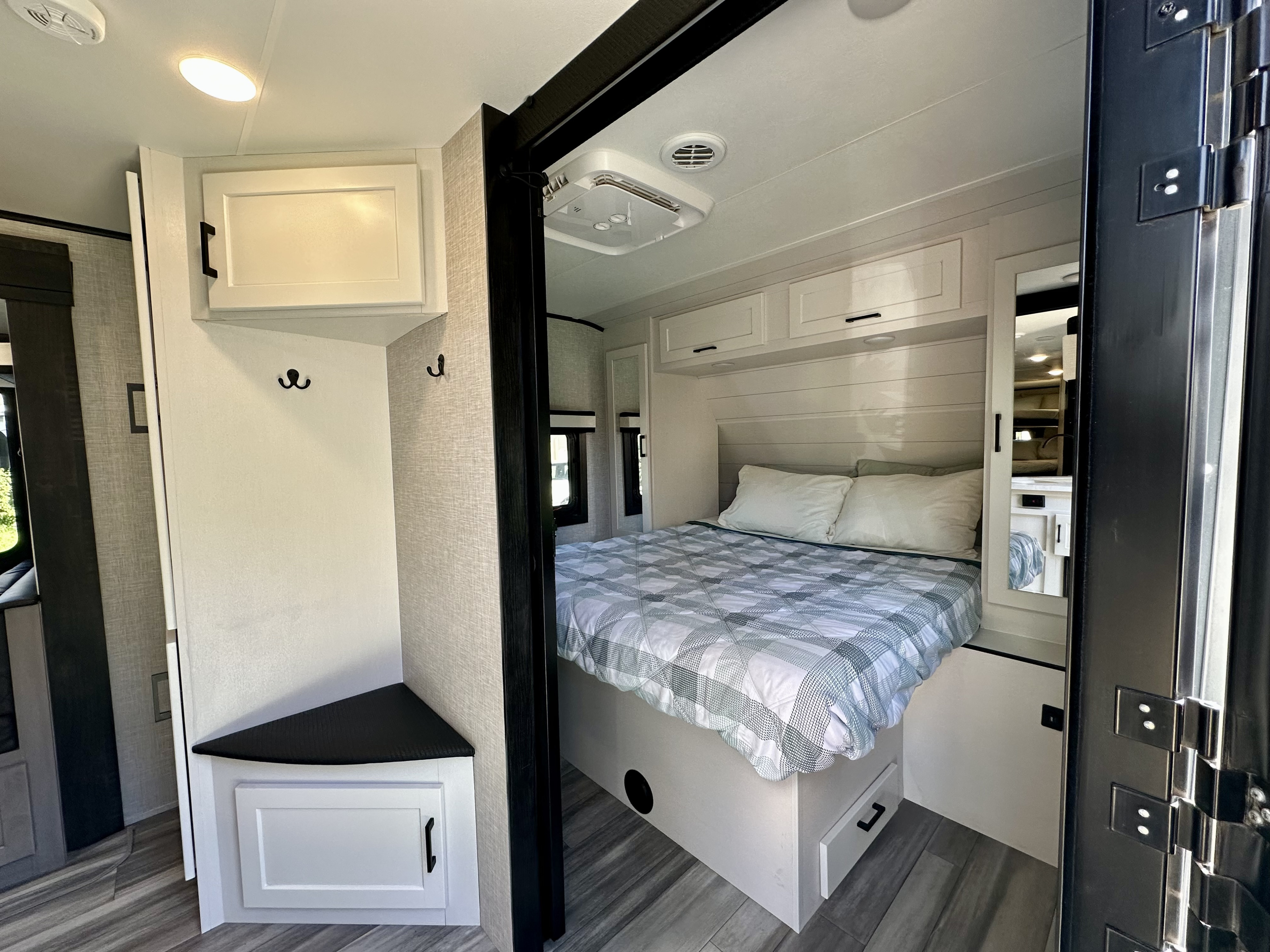 Modern rv rental bedroom: bed with plaid comforter, white cabinets, corner storage, and a mirror.. Jayco Jay Feather 2024