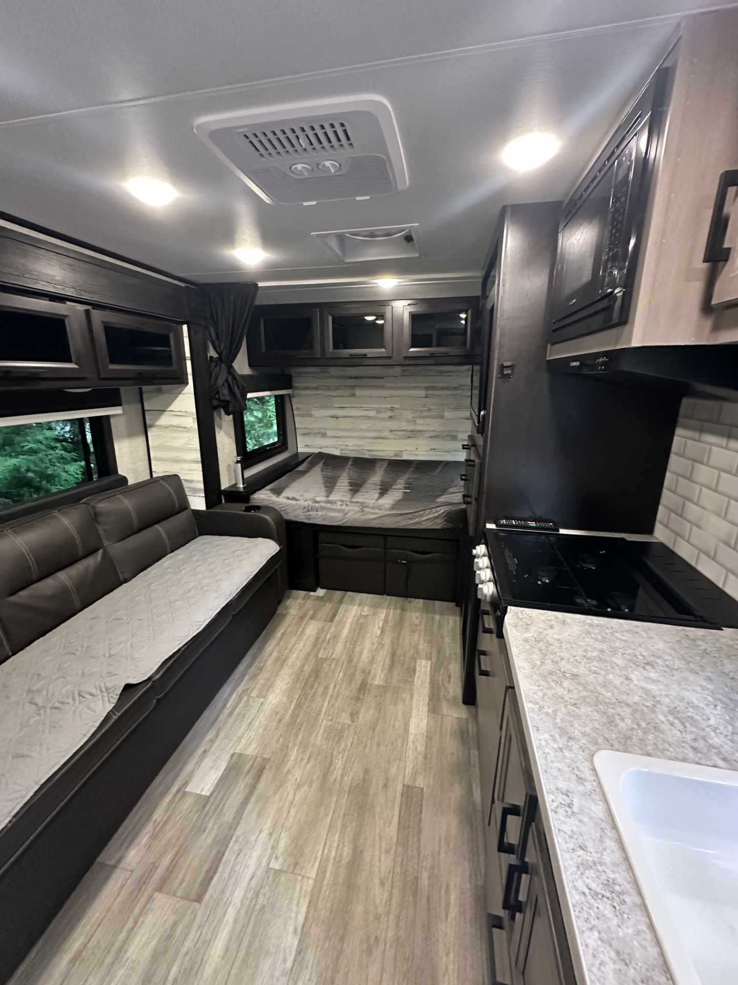 This modern RV rental features a comfortable living area with a dark leather couch, a compact kitchen with a stovetop and sink, and a cozy bed space in the rear, all within a well-lit interior.. Jayco Jay Feather Micro 2022
