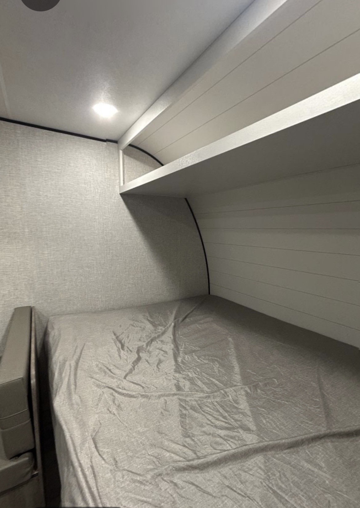 Inside an RV rental: a neat sleeping bunk with a built-in shelf, overhead light, and grey bedding.. Aspen Trail Open Range Conventional 2025