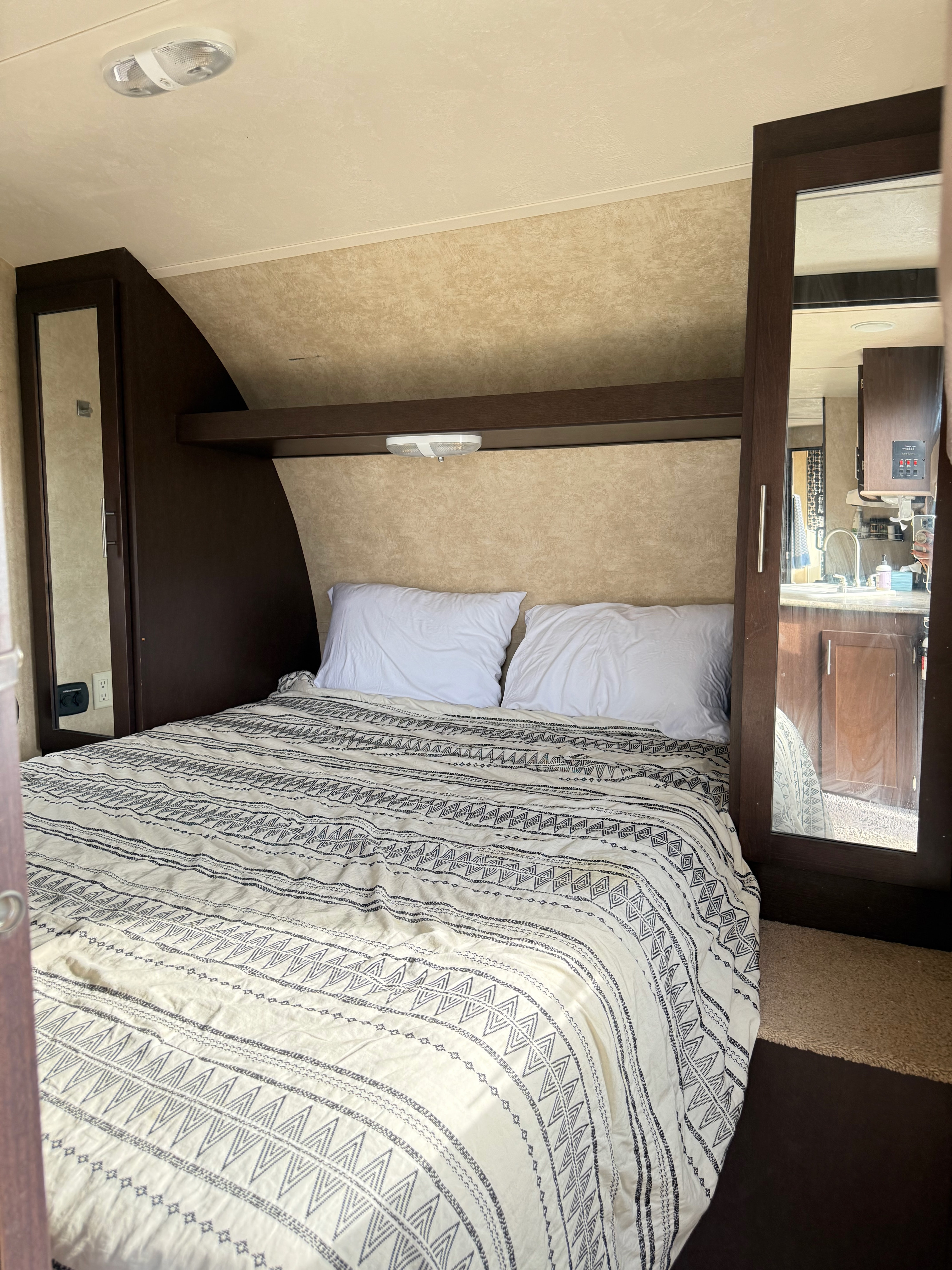 Cozy RV rental bedroom featuring a bed with a patterned duvet, two white pillows, dark wood cabinetry, and an overhead light.. Forest River EVO T2850 2016