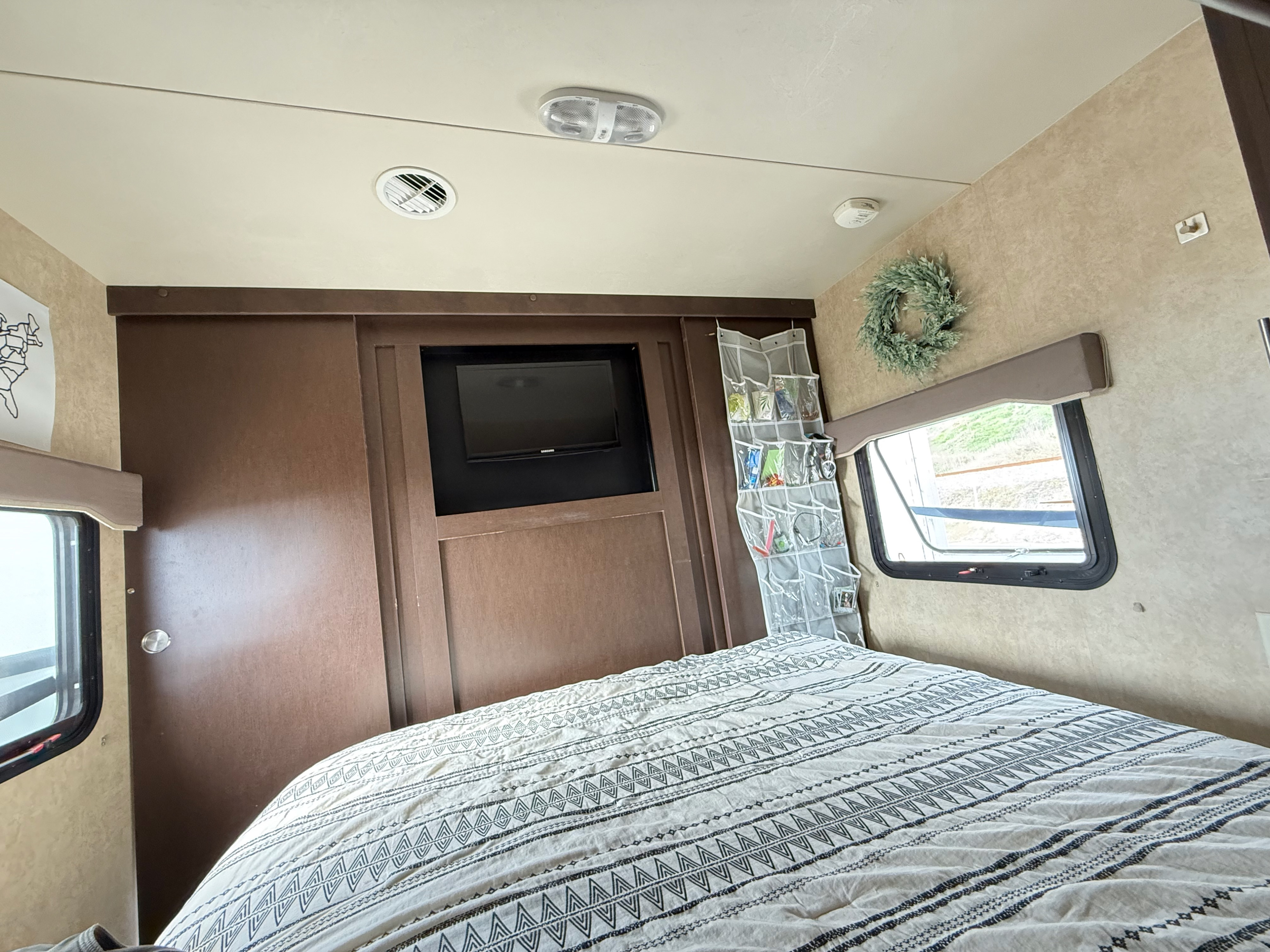 An RV rental bedroom interior showcasing a comfy bed, TV, window, and practical hanging storage.. Forest River EVO T2850 2016