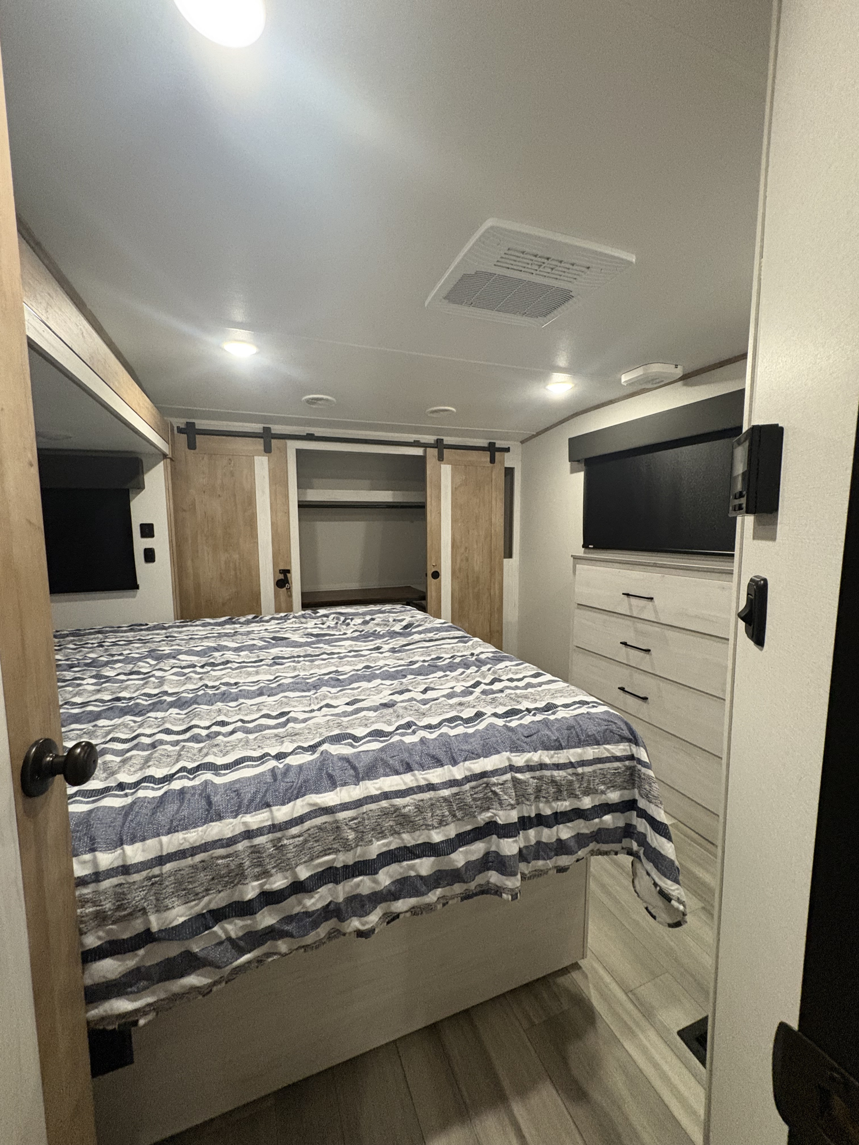 Modern RV rental bedroom with a comfortable striped bed, wooden barn door closet, and dresser for storage.. Heartland RVs Milestone 2024