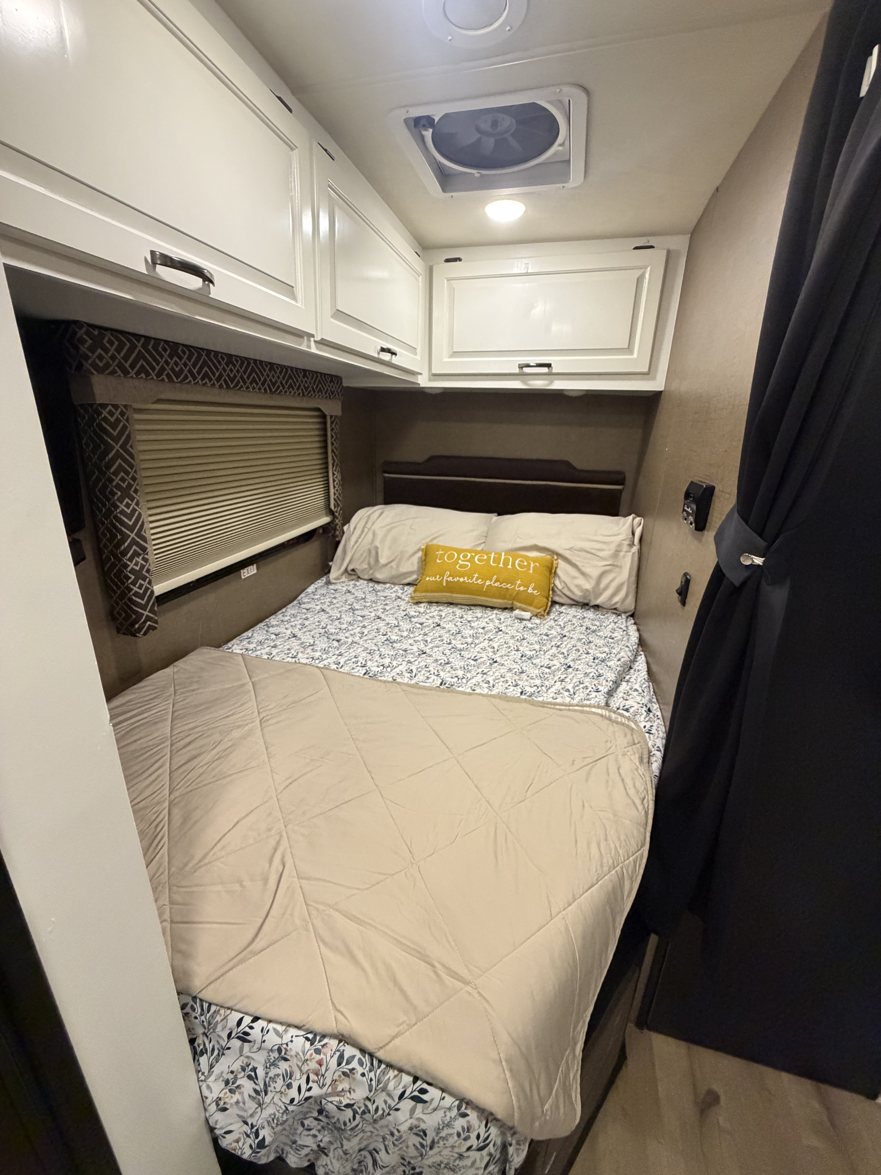This RV rental bedroom features a comfy bed with floral sheets, overhead cabinets, and a window for a cozy travel experience.. Thor Four Winds 2018