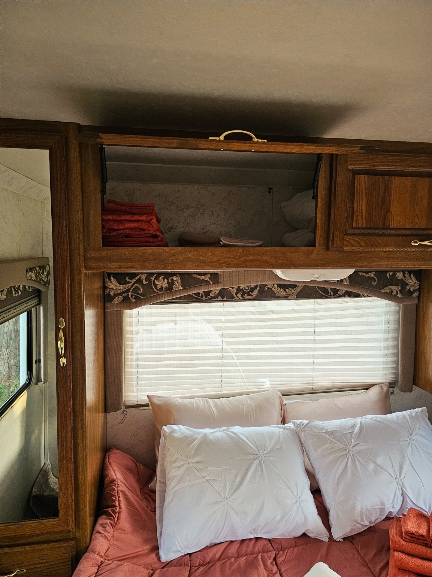 Cozy RV rental bedroom featuring a comfortable bed with pillows, a window with blinds, and overhead storage with towels.. Thor Motor Coach 31E 2002