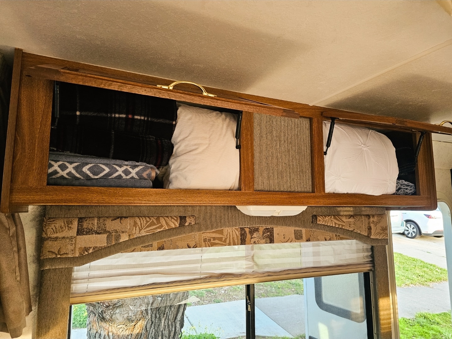 **RV rental** interior features open overhead wood cabinets, neatly storing blankets & pillows above a window with blinds.. Thor Motor Coach 31E 2002