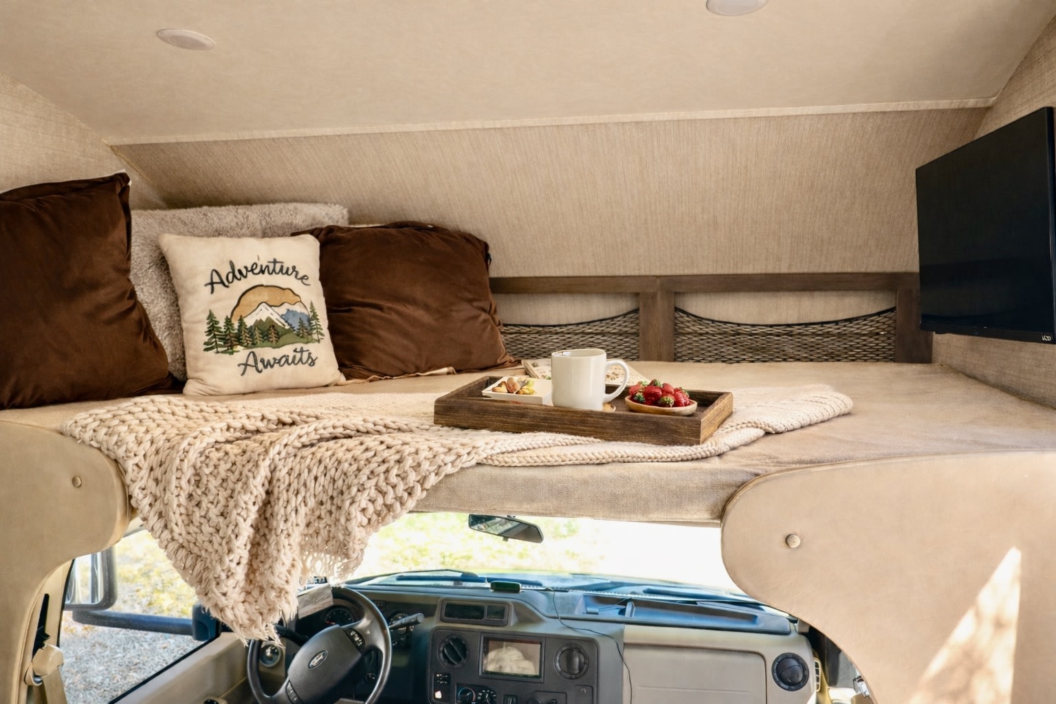 Cozy RV rental over-cab bunk with "Adventure Awaits" pillow, breakfast, blanket, and TV for ultimate comfort.. Jayco Redhawk 2020