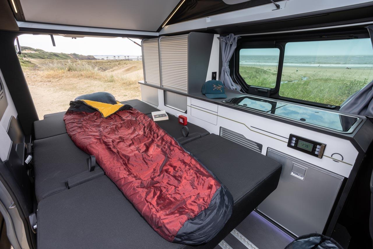 Cozy camper van RV rental interior featuring a bed, compact kitchen, and a beautiful beach view for your next travel adventure.. Handroad 2026 2026