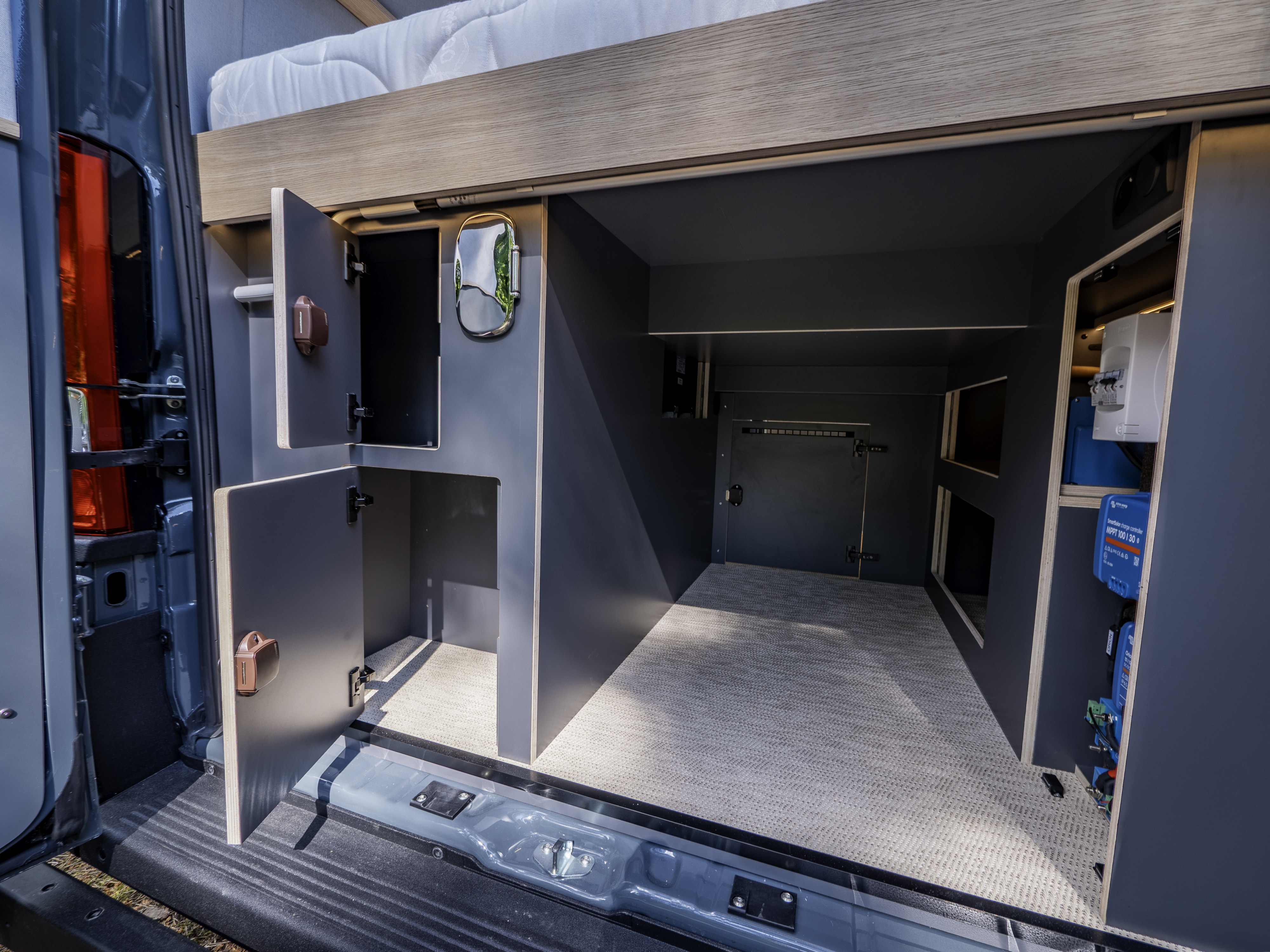 Spacious RV rental camper van storage 'garage' area with overhead bed, open cabinets, and visible electrical system.. Fiat Ducato 2025