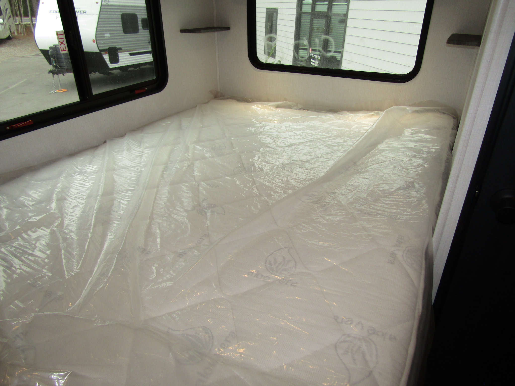 Inside an RV rental, a new, plastic-wrapped mattress with "Aloe Vera" text is ready. Windows reveal the exterior.. Forest River Sunseeker LE 2026