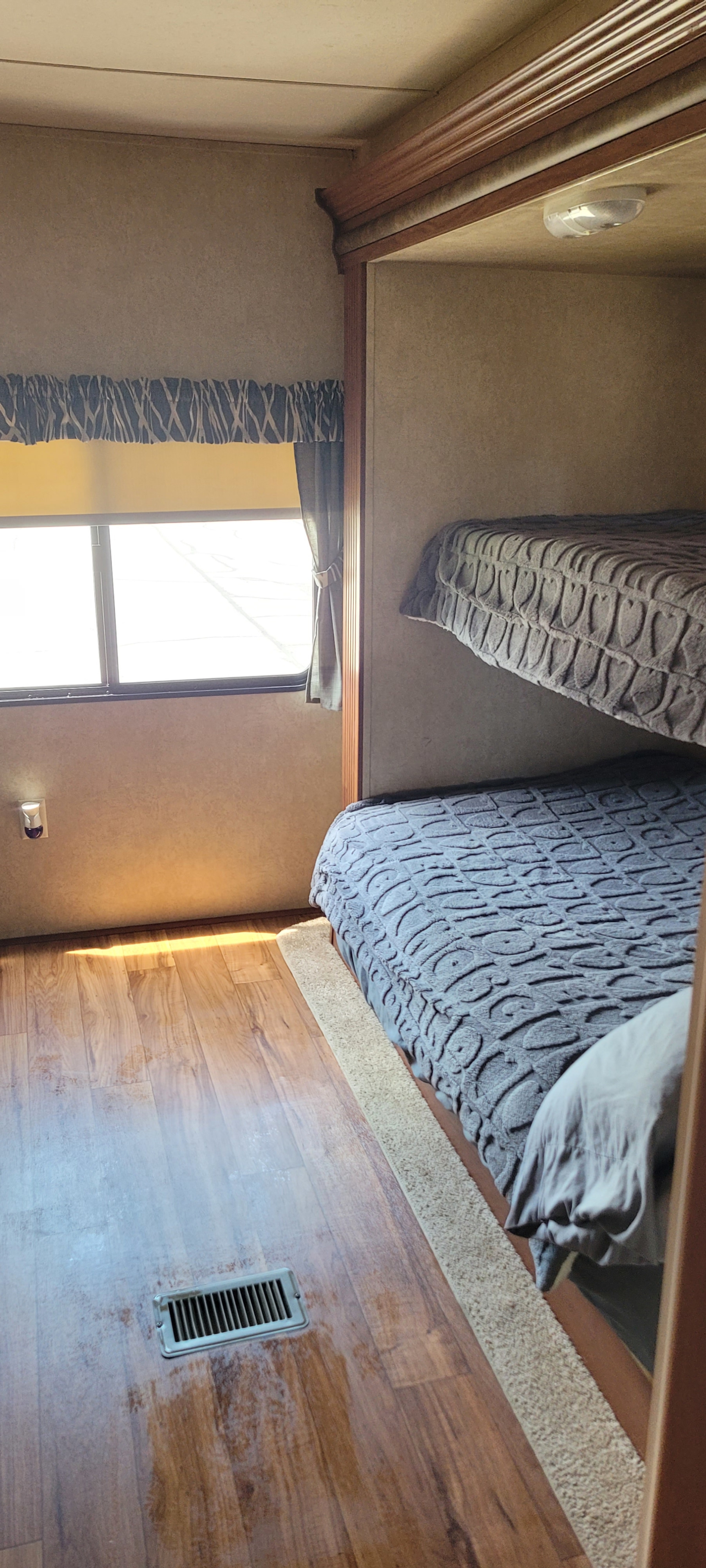 Cozy RV rental bunk bedroom features two comfy beds, a bright window, and wood-look flooring for travel accommodations.. Forest River Salem 2014