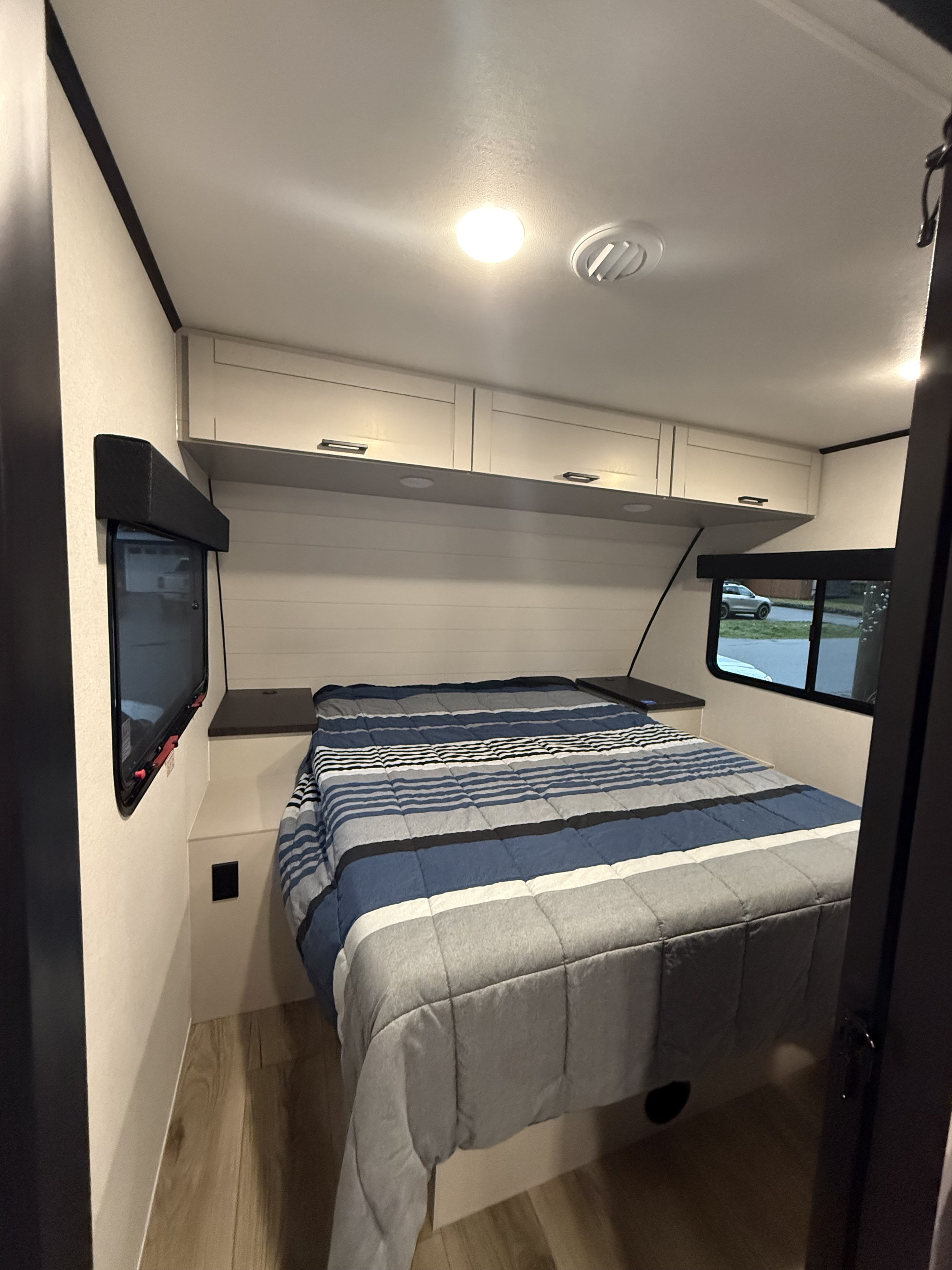 This RV rental bedroom features a comfy bed with a striped comforter, overhead cabinets, and a window for a cozy stay.. Jayco Jayfeather 2026