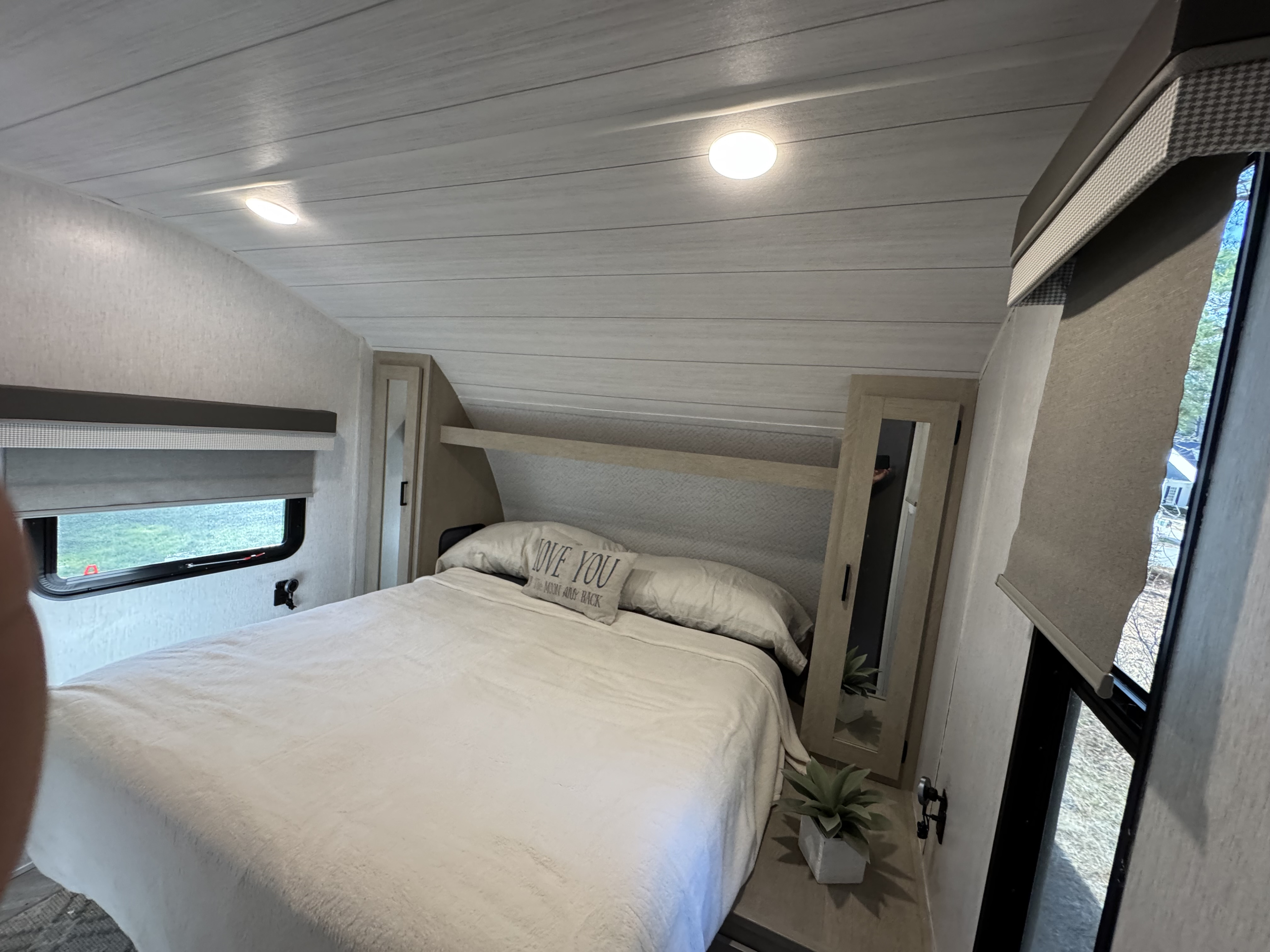Modern rv rental bedroom with light planked ceiling, comfortable white bed, window blinds, and built-in storage.. Forest River Wildwood X-Lite Platinum 2023