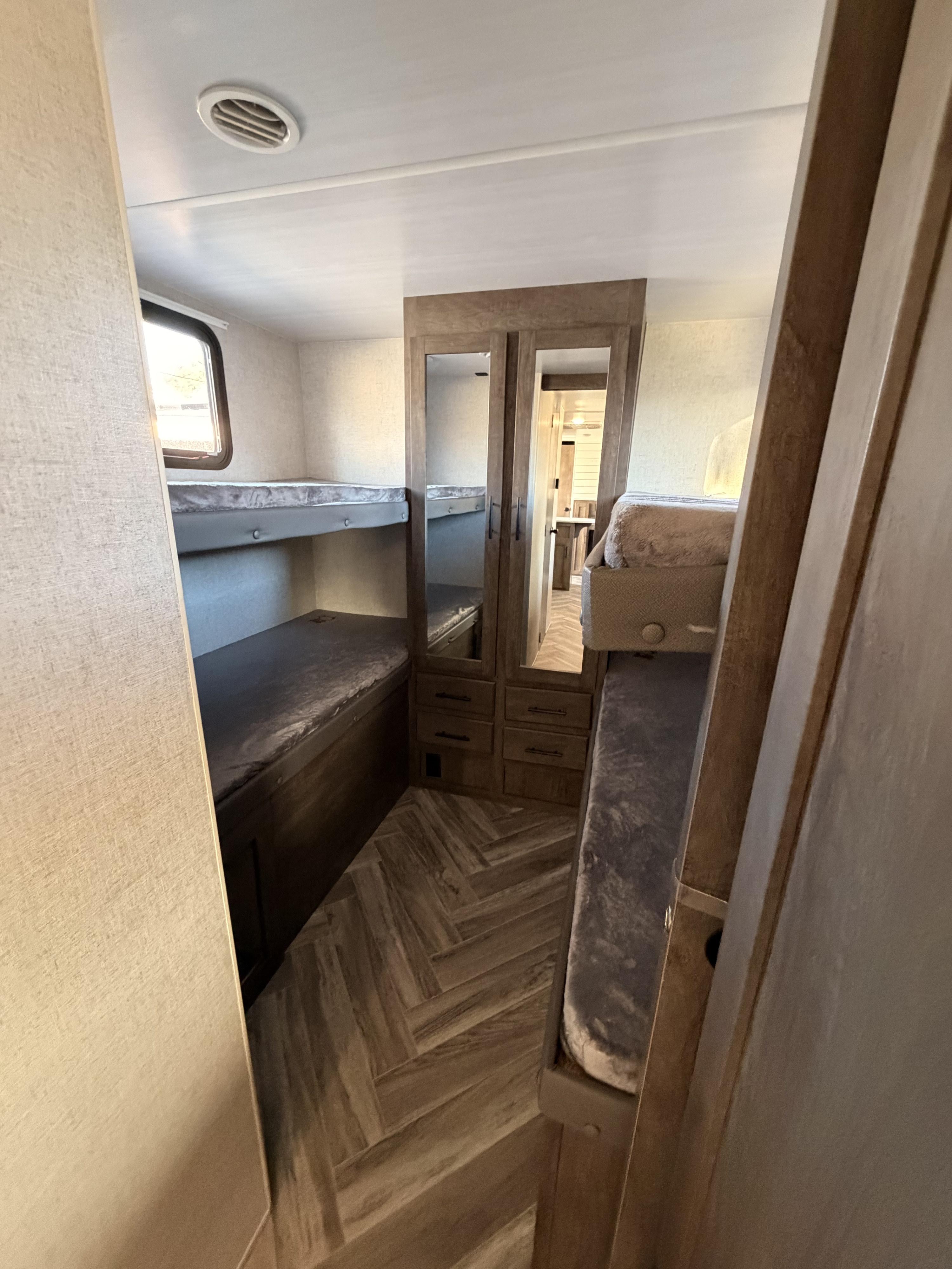 Inside an RV rental, this bunkhouse features two sets of beds, a central mirrored closet with drawers, and herringbone wood-look flooring.. Forest River Wildwood X-Lite 2021