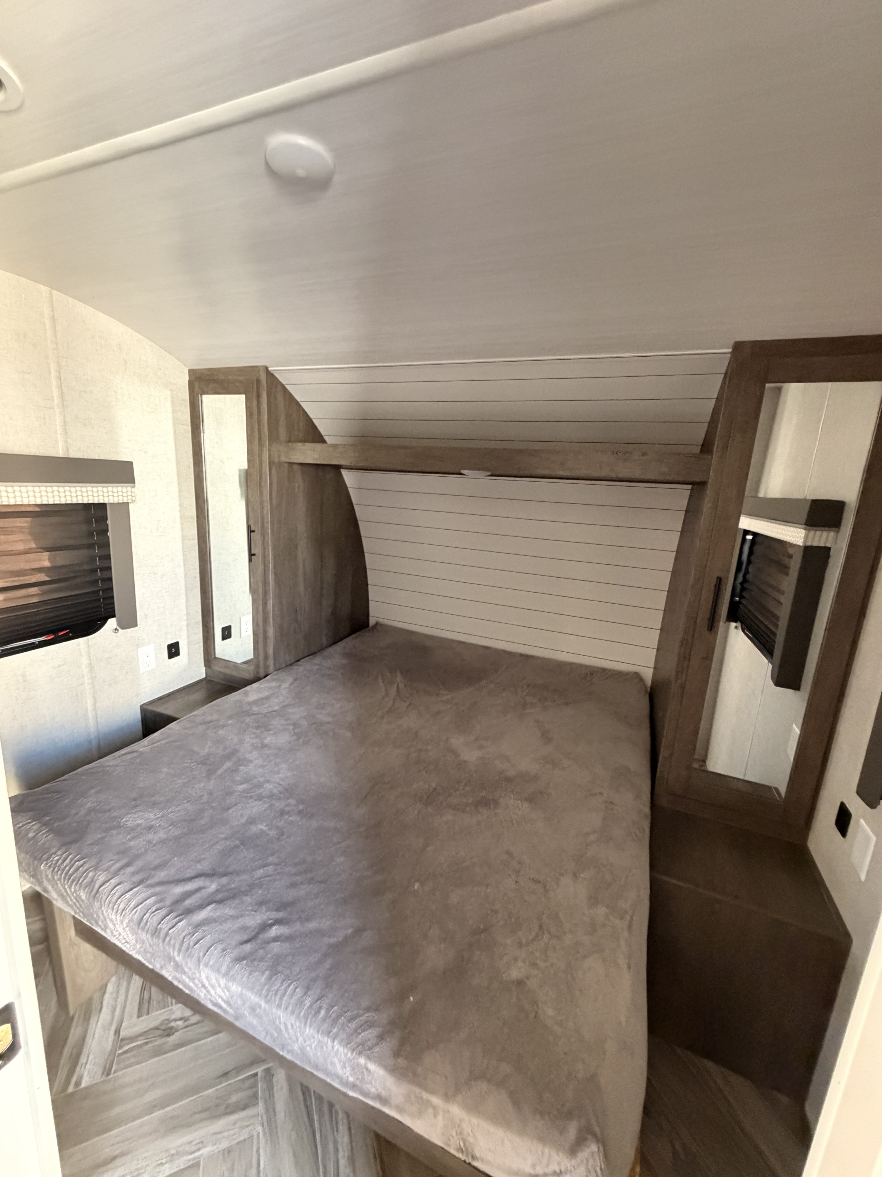 RV rental bedroom with a comfortable grey bed, mirrored wardrobes, window blinds, and light wood furniture.. Forest River Wildwood X-Lite 2021