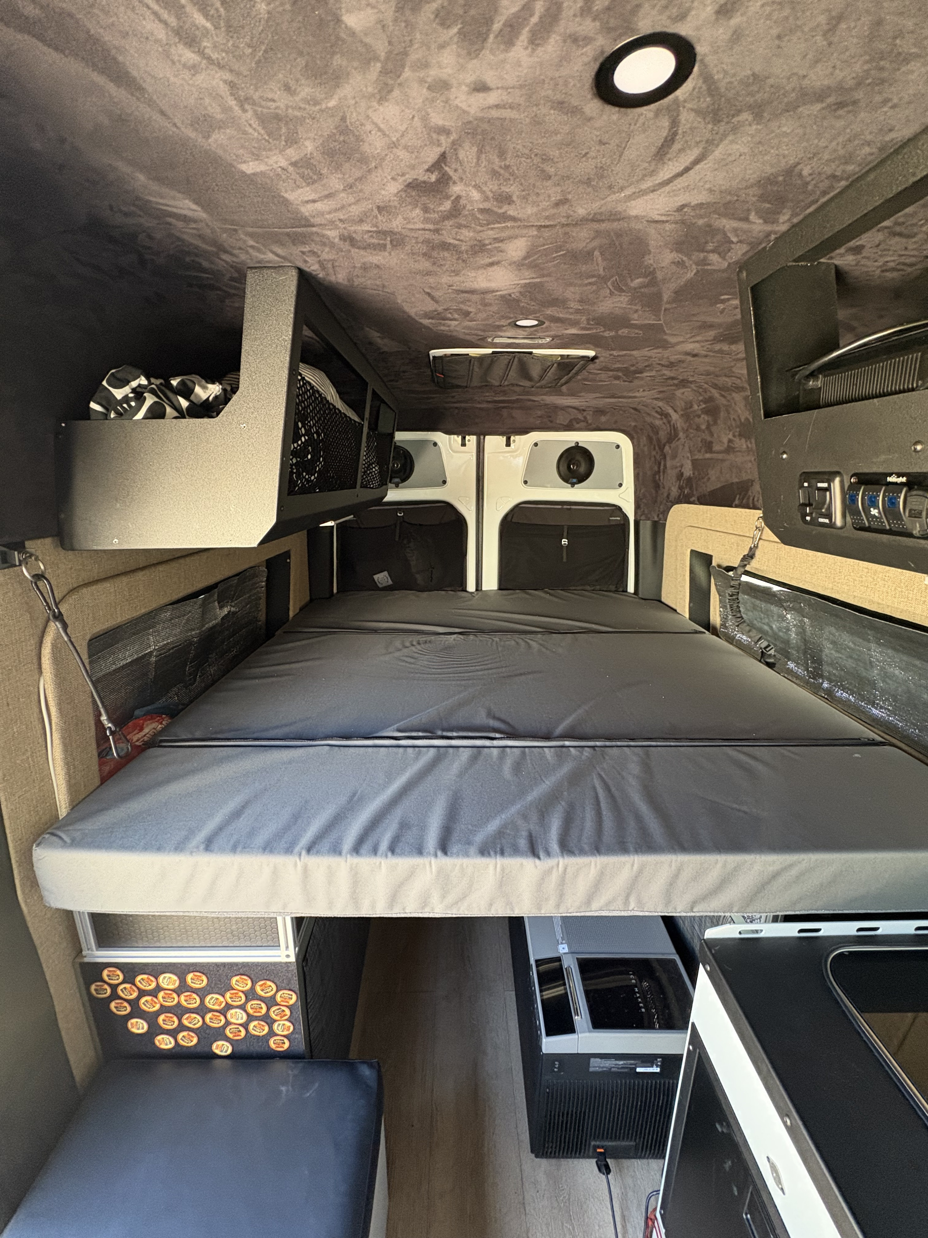 Spacious RV rental interior with a large bed, overhead storage, integrated speakers, and an ice maker, ready for adventure.. Mercedes Sprinter Sprinter 144 2017