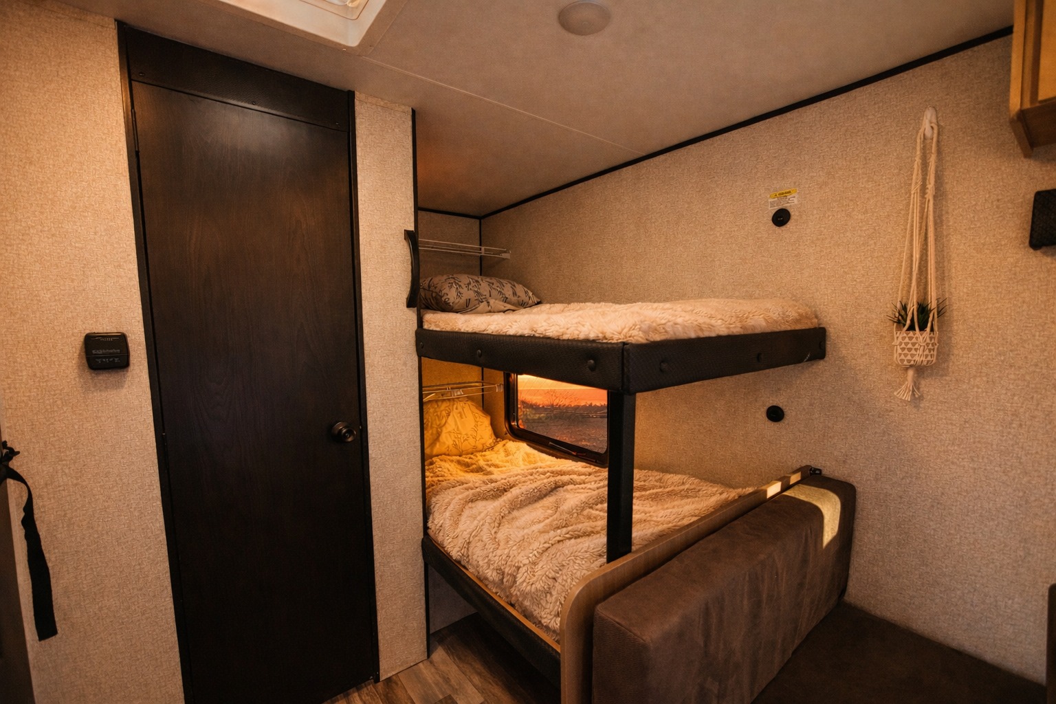 Cozy RV rental bunk beds with a window revealing a sunset view, adjacent to a dark door and thermostat.. Jayco 170BHW SLX Sport 2026
