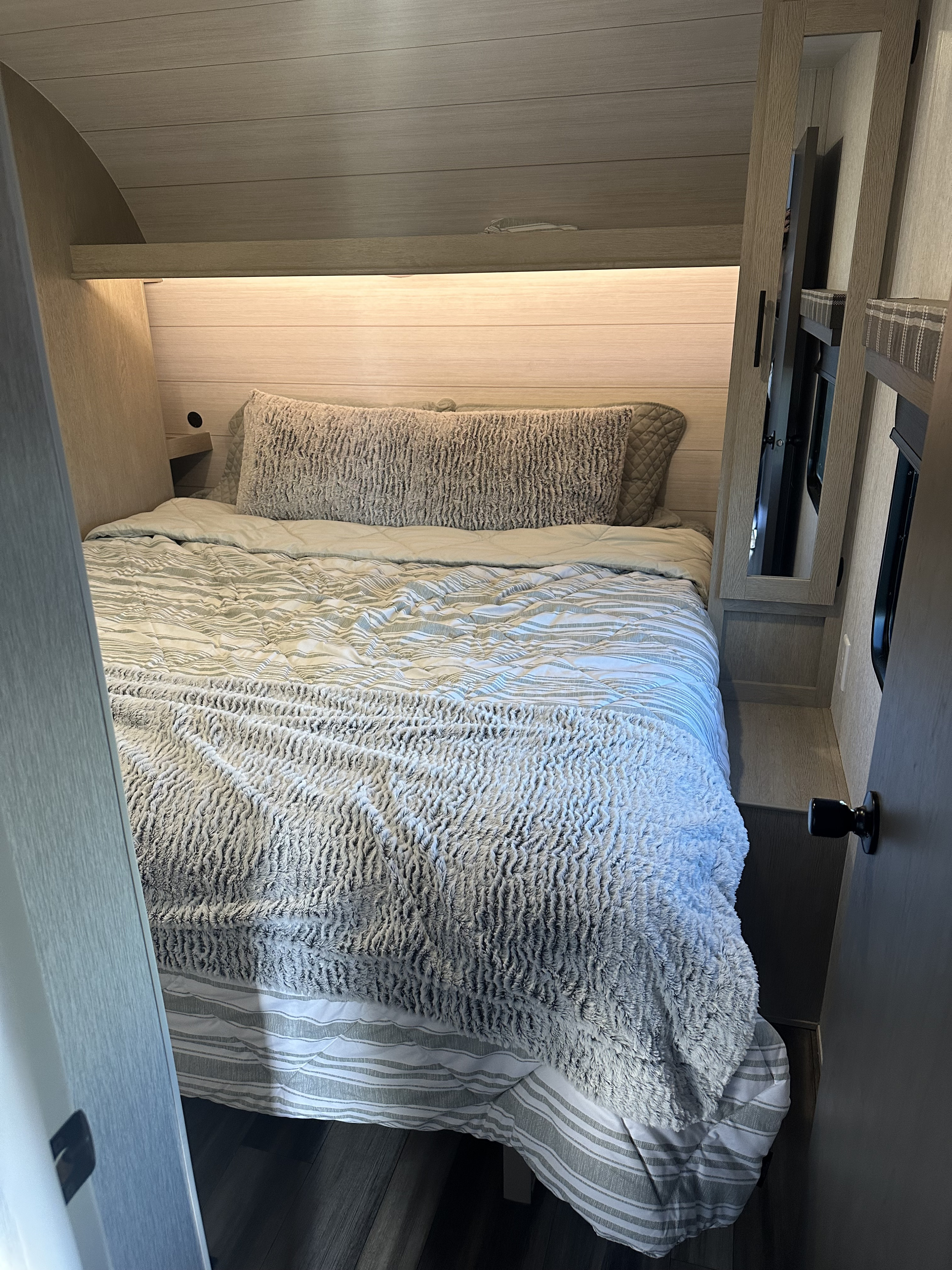 Cozy RV rental bedroom features a comfy bed with striped comforter, plush blanket, and modern wood paneling with ambient lighting.. Forest River Stealth 2024