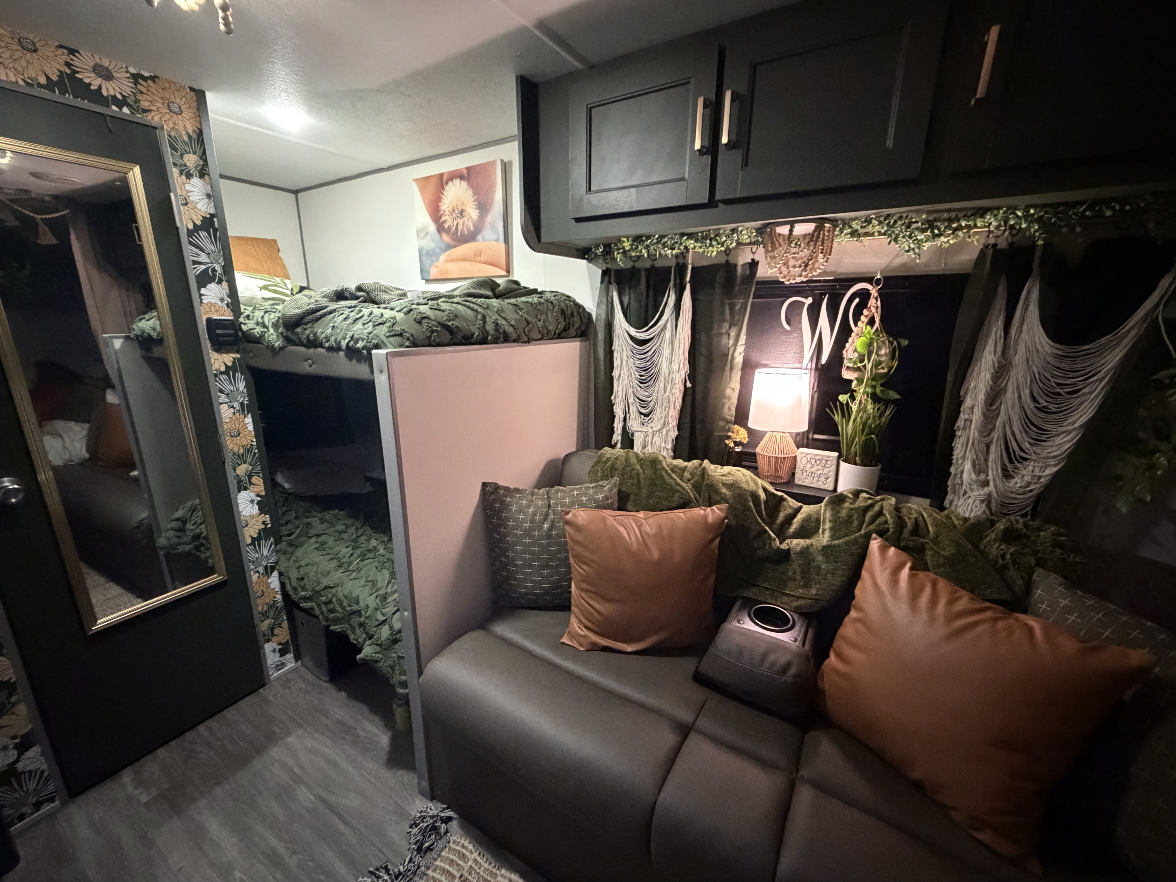 Cozy RV rental interior: dark green bunks, sofa with brown pillows, floral accents, and macrame decor.. Forest River Aurora Aurora Light 2024