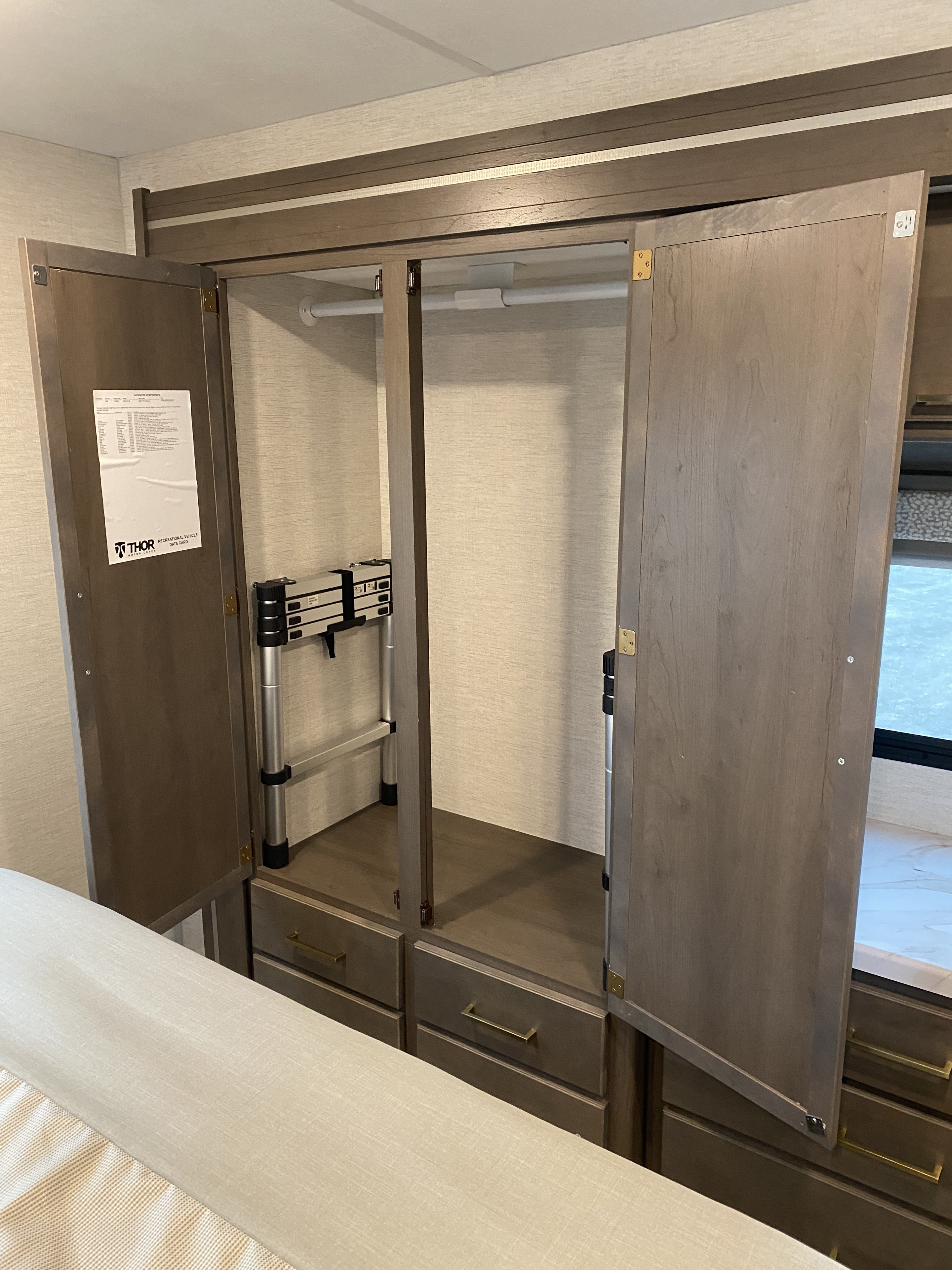 RV rental interior showing a large open wardrobe with a hanging rod, drawers, and a collapsible ladder.. Thor Chateau 2025