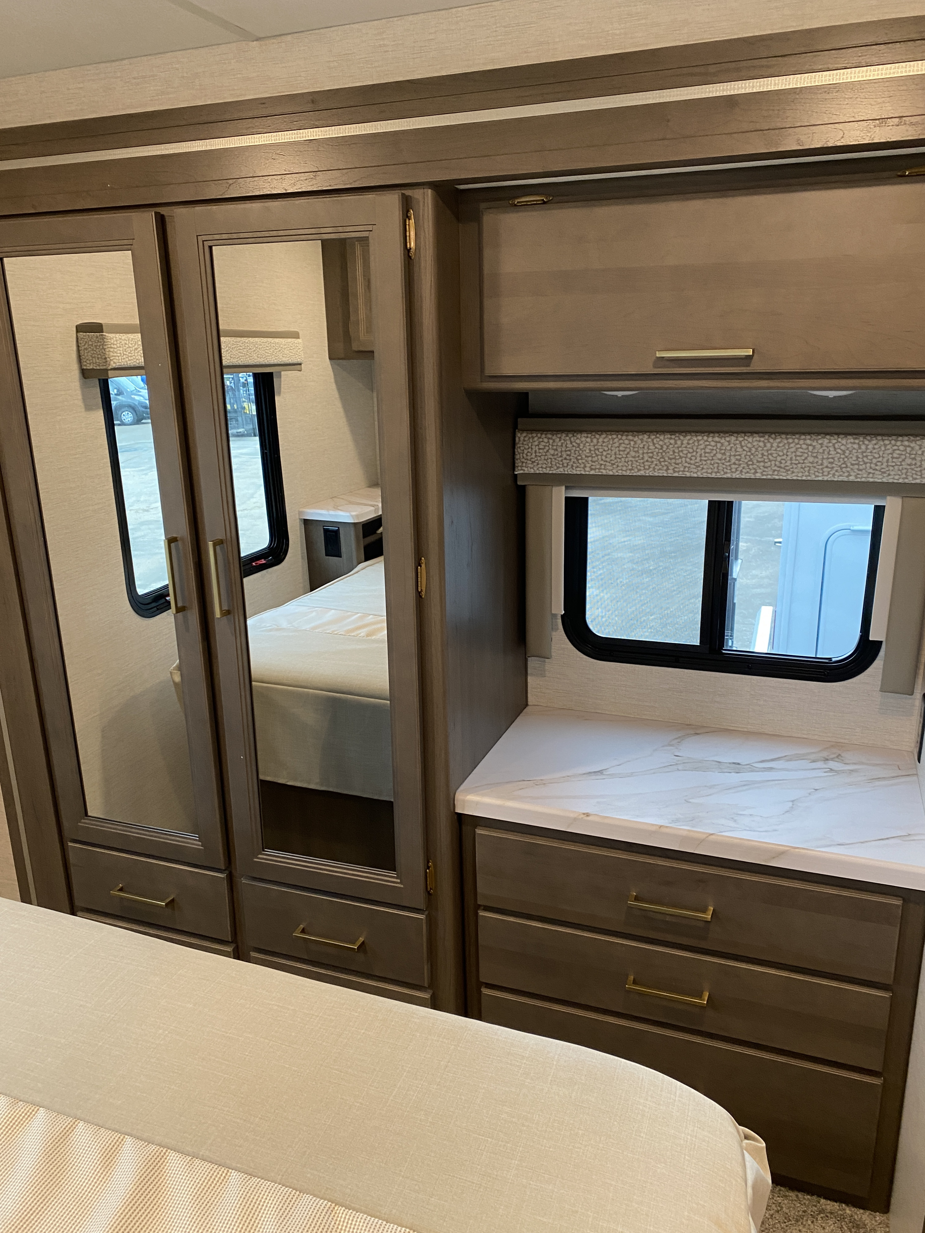 Inside a comfortable RV rental bedroom, featuring a mirrored wardrobe, dresser with countertop, and a window.. Thor Chateau 2025