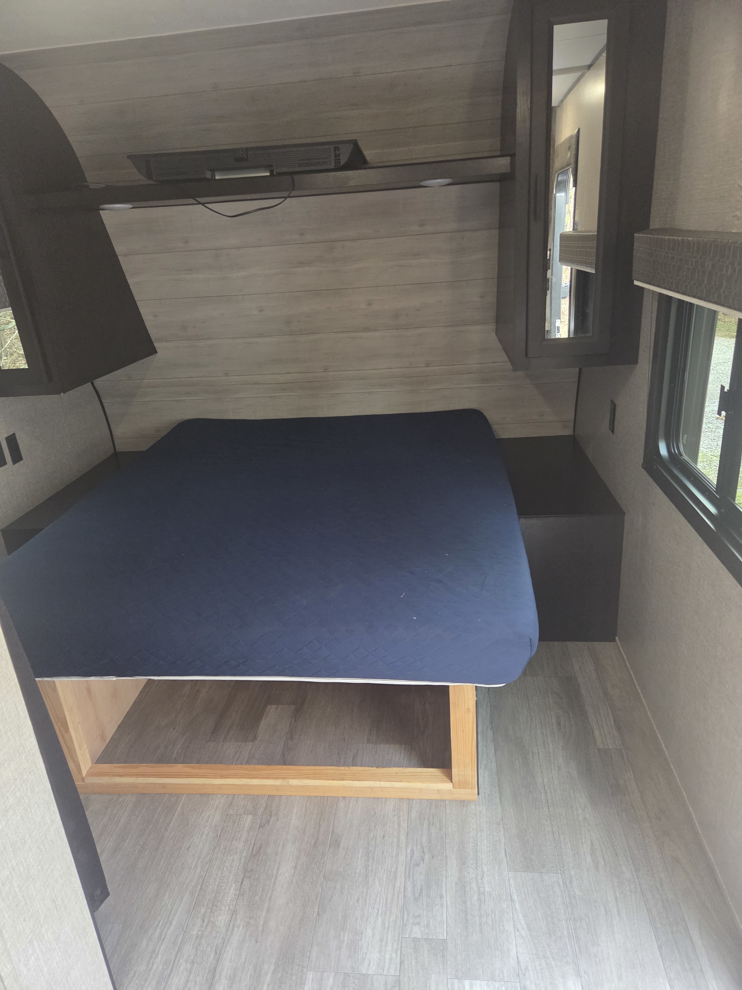 An RV rental bedroom with a blue bed, light wood-look interior walls, overhead storage, and a mounted TV. Ready for travel.. Jayco Jay Flight SLX 2022