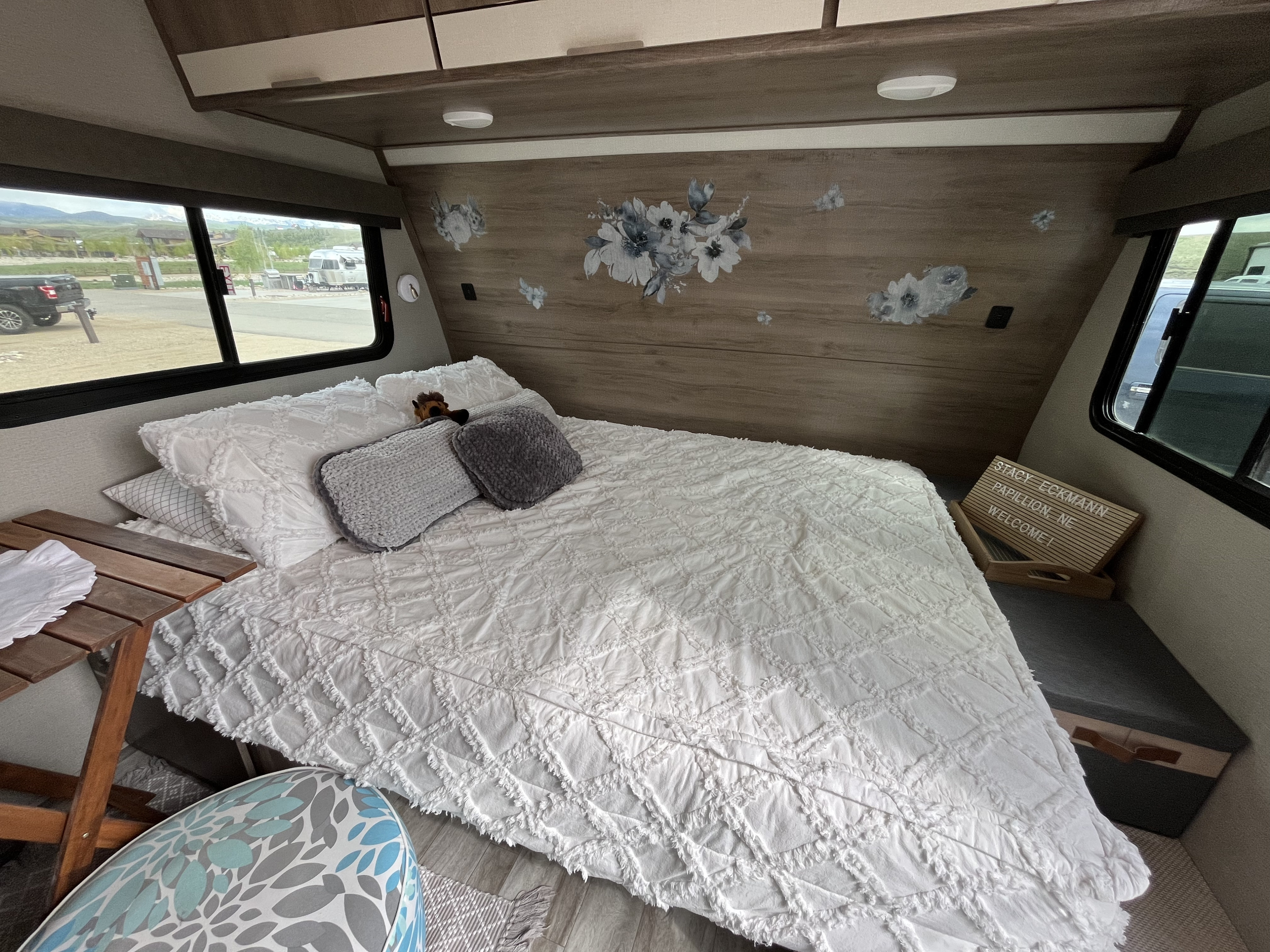 Inside a cozy rv rental, this bedroom features a comfy white bed, decorative wall, welcome sign, and campground views.. Grand Design Imagine XLS 2021
