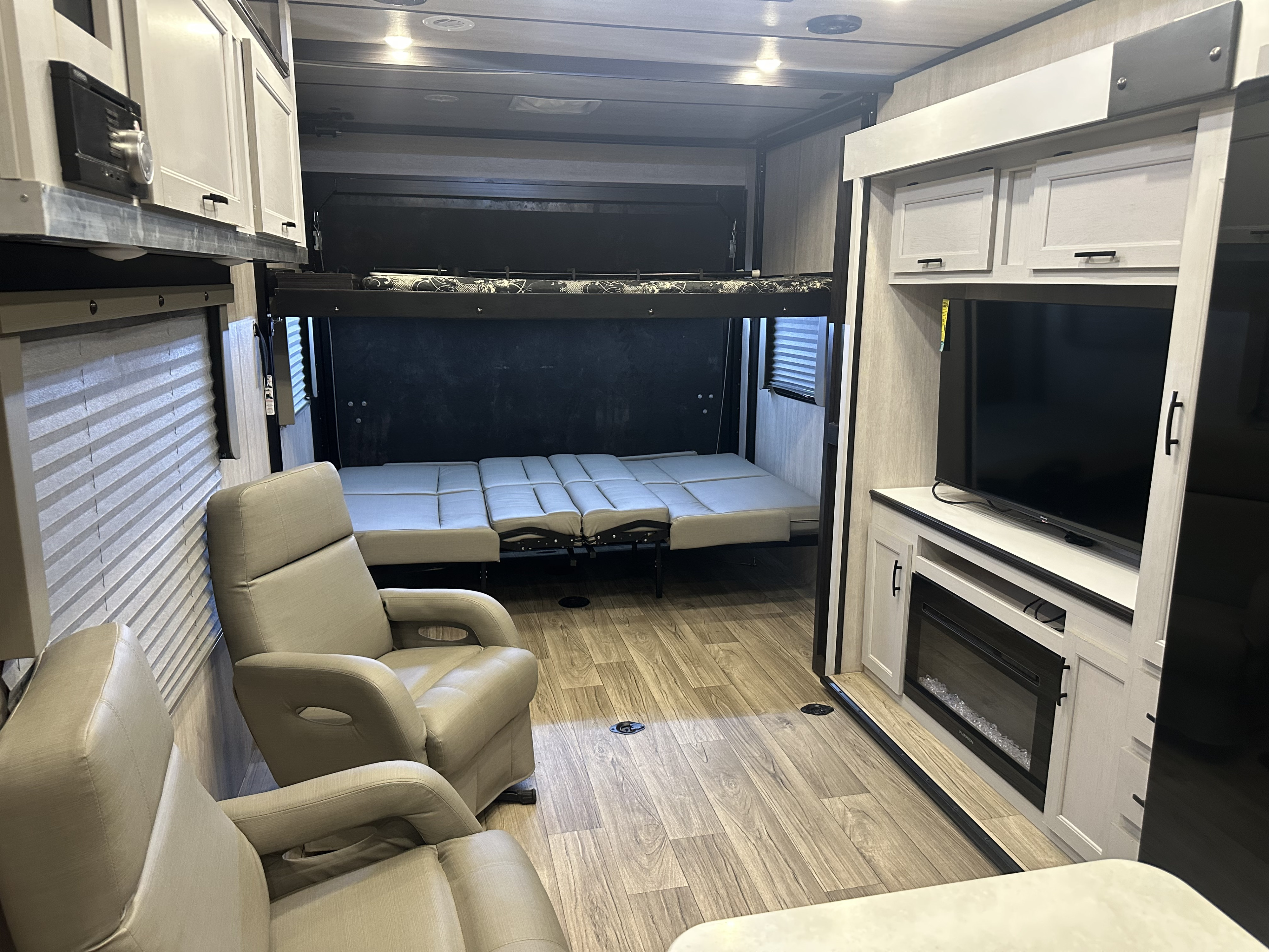 This RV rental toy hauler interior features recliners, convertible bunk beds/sofa, a TV, and a fireplace, creating a versatile living space.. Genesis Supreme Rv Genesis Supreme 2025