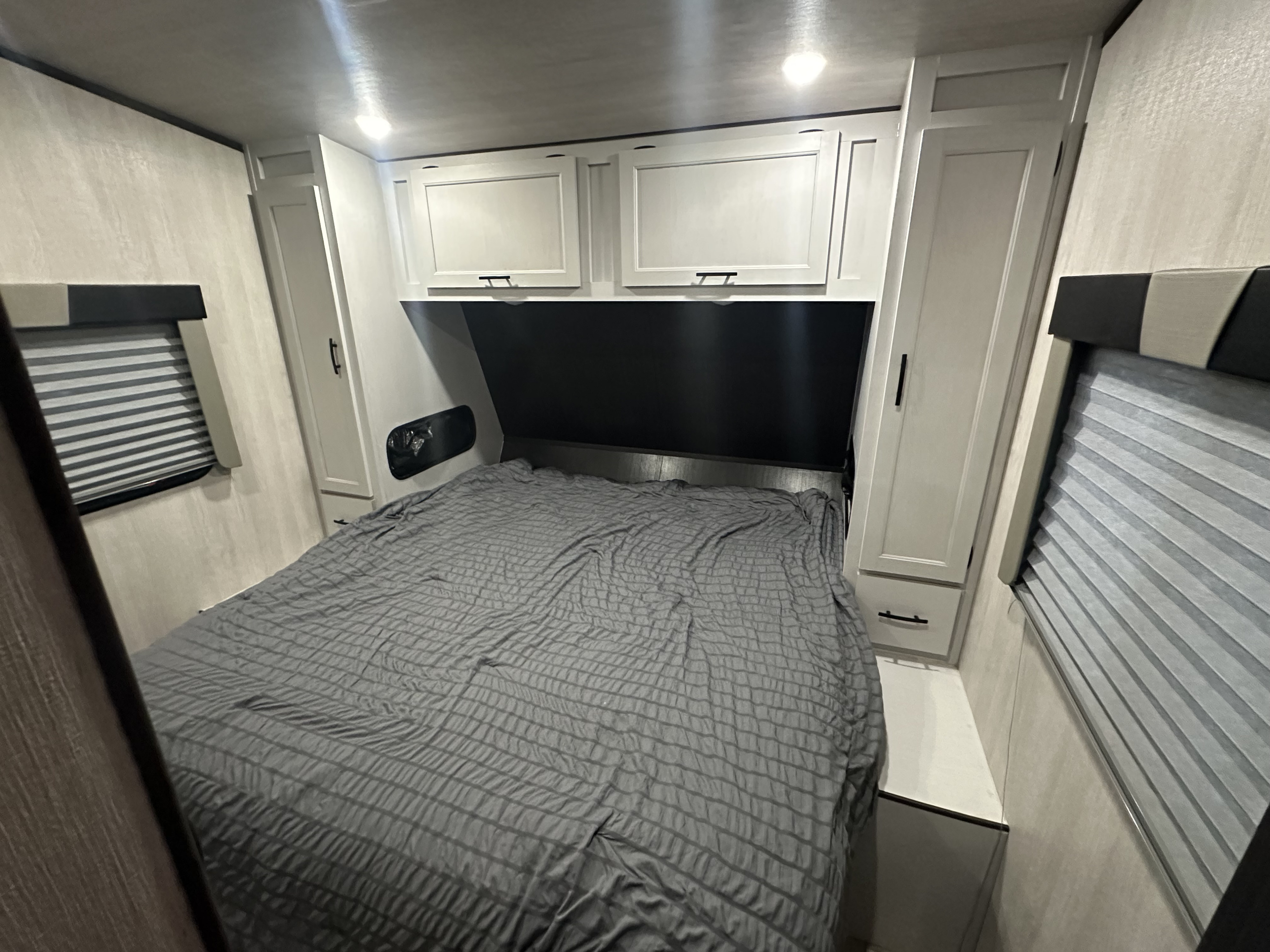 Comfortable RV rental bedroom with a large grey bed, overhead cabinets, and side wardrobes. Windows with blinds offer privacy.. Genesis Supreme Rv Genesis Supreme 2025