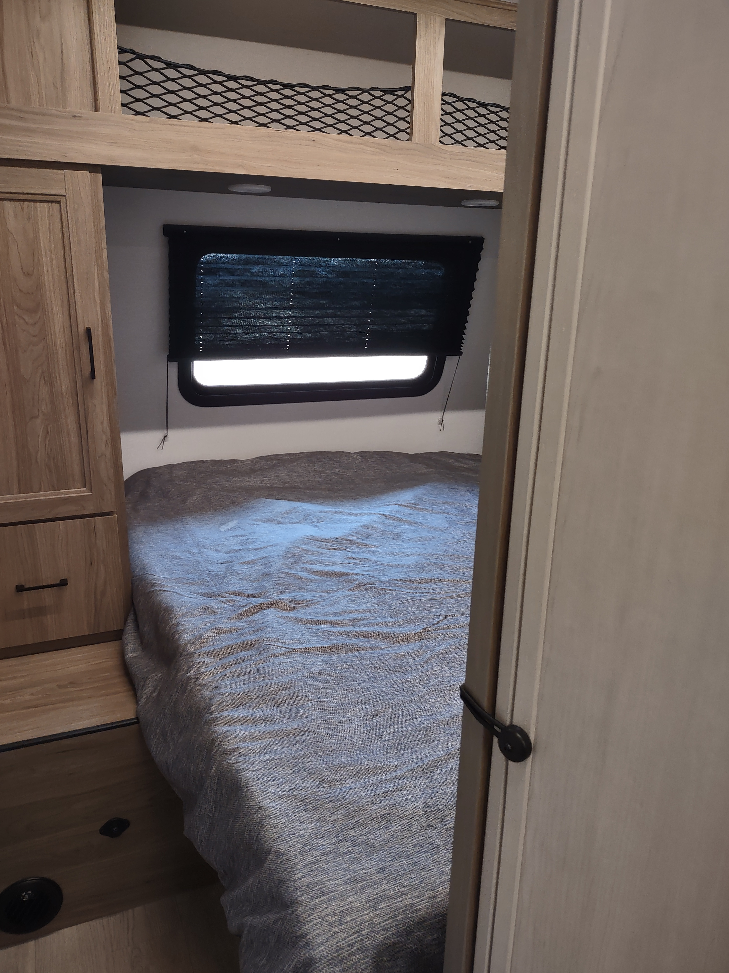 RV rental bedroom: a cozy bed, window with blind, wooden cabinet, and an upper bunk with safety netting, seen from a doorway.. Coachmen 29 SE 2025