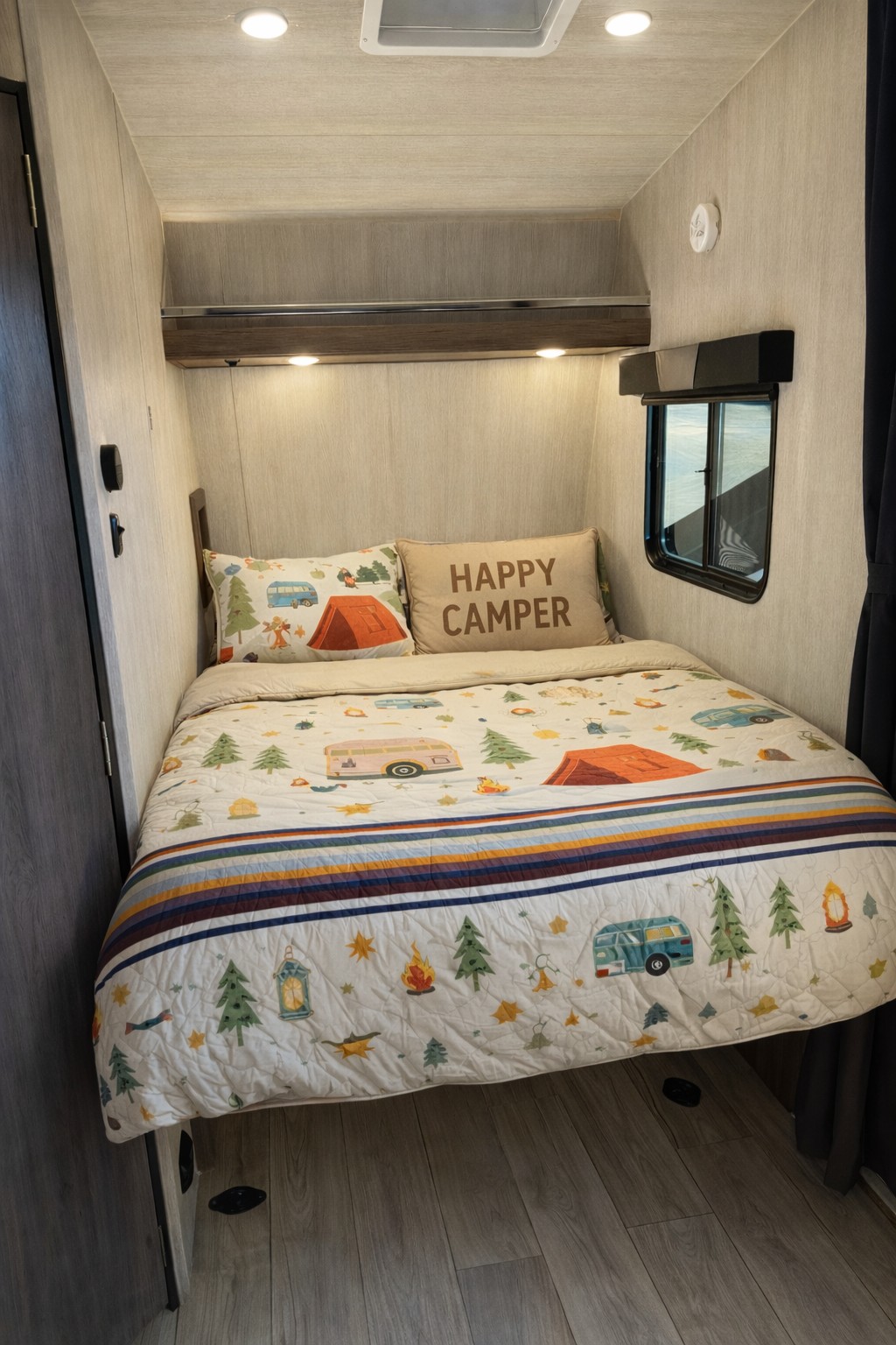 This RV rental bedroom features a bed with camping-themed bedding, 'HAPPY CAMPER' pillow, and small window. Cozy travel space.. Genesis Supreme Rv Genesis Supreme 2026
