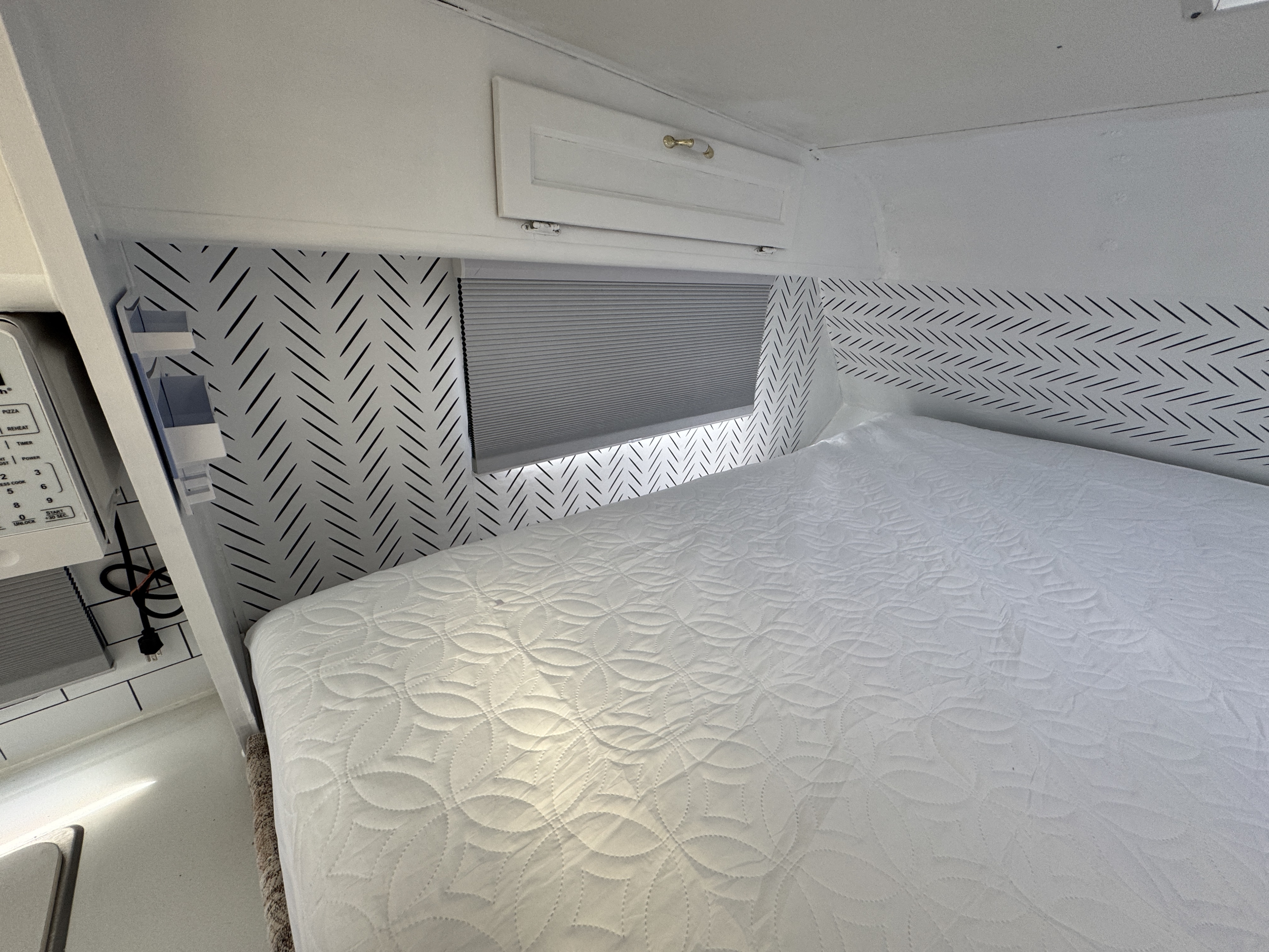 Cozy RV rental bedroom featuring a white quilted bed, herringbone wallpaper, and compact kitchen area with a microwave.. Western Rv 2014 f150. 6 seats 1999