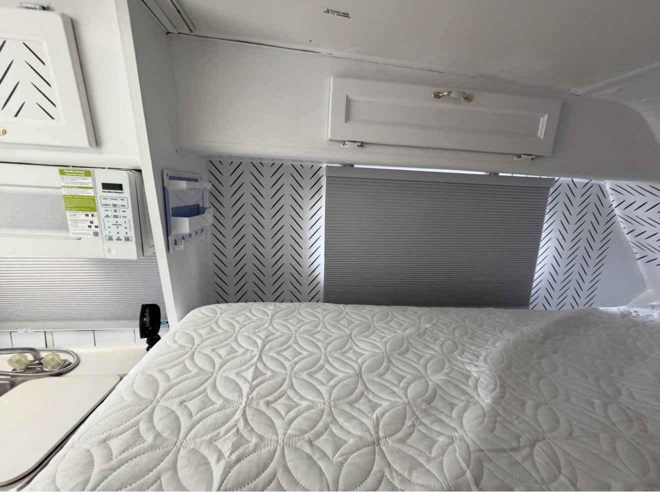 Clean and cozy RV rental bedroom with white quilted bed, microwave, and herringbone accent walls.. Western Rv 2014 f150. 6 seats 1999