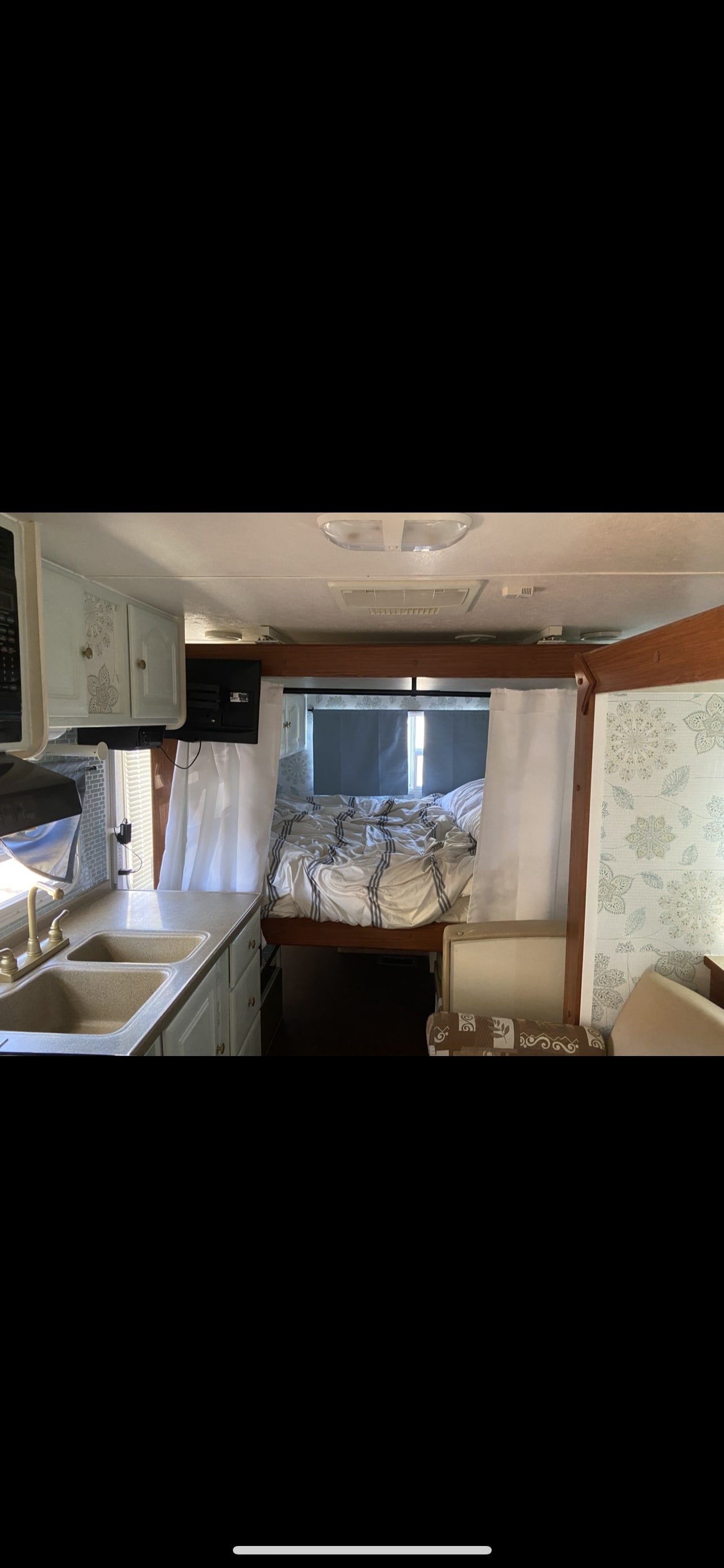 Inside an RV rental: kitchen with sink, mounted TV, bed with striped bedding, and patterned wall.. Malibu Malibu Trailer 2008