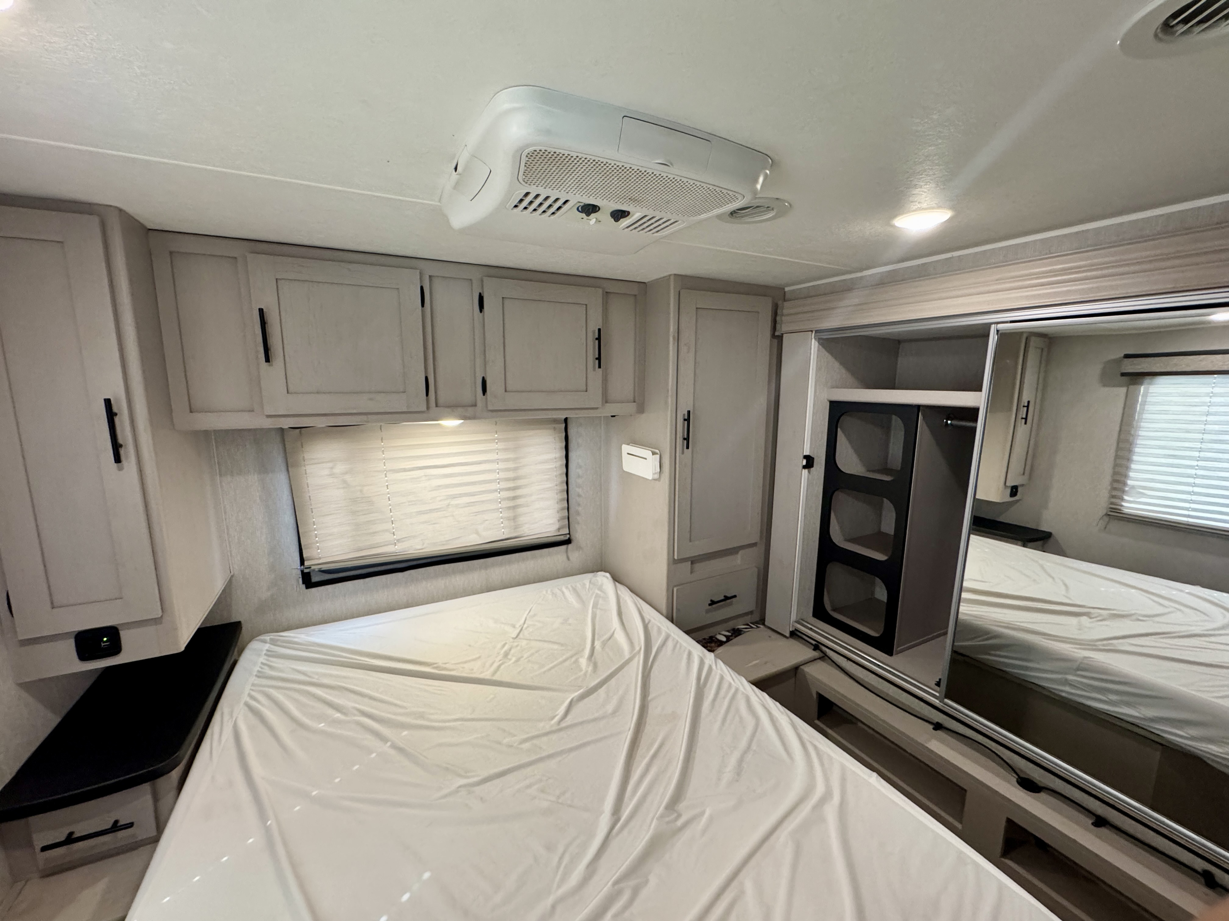 Cozy RV rental bedroom featuring a comfortable bed, window with blinds, overhead storage, air conditioner, and mirrored closet.. Forest River Coachmen Freelander 2023