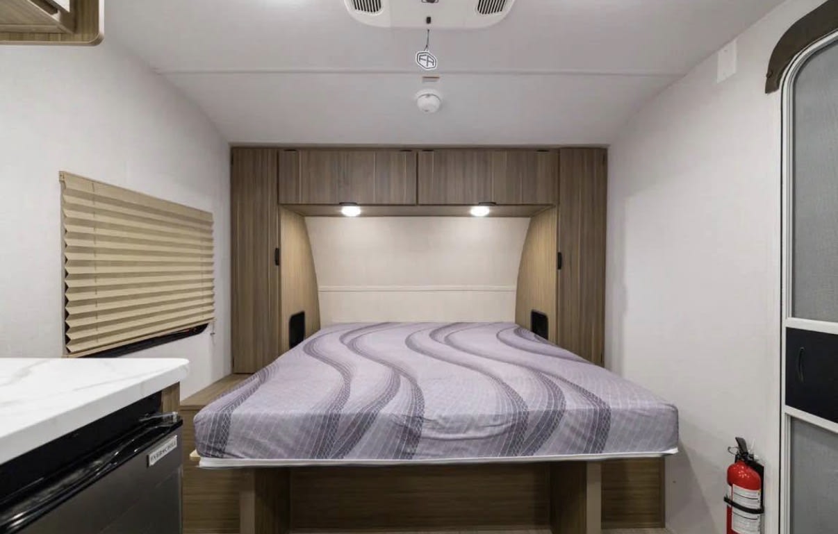 RV rental bedroom: Features a bed, overhead storage, window with blinds, AC, and a fire extinguisher for safe travels.. Forest River Salem FSX 2026