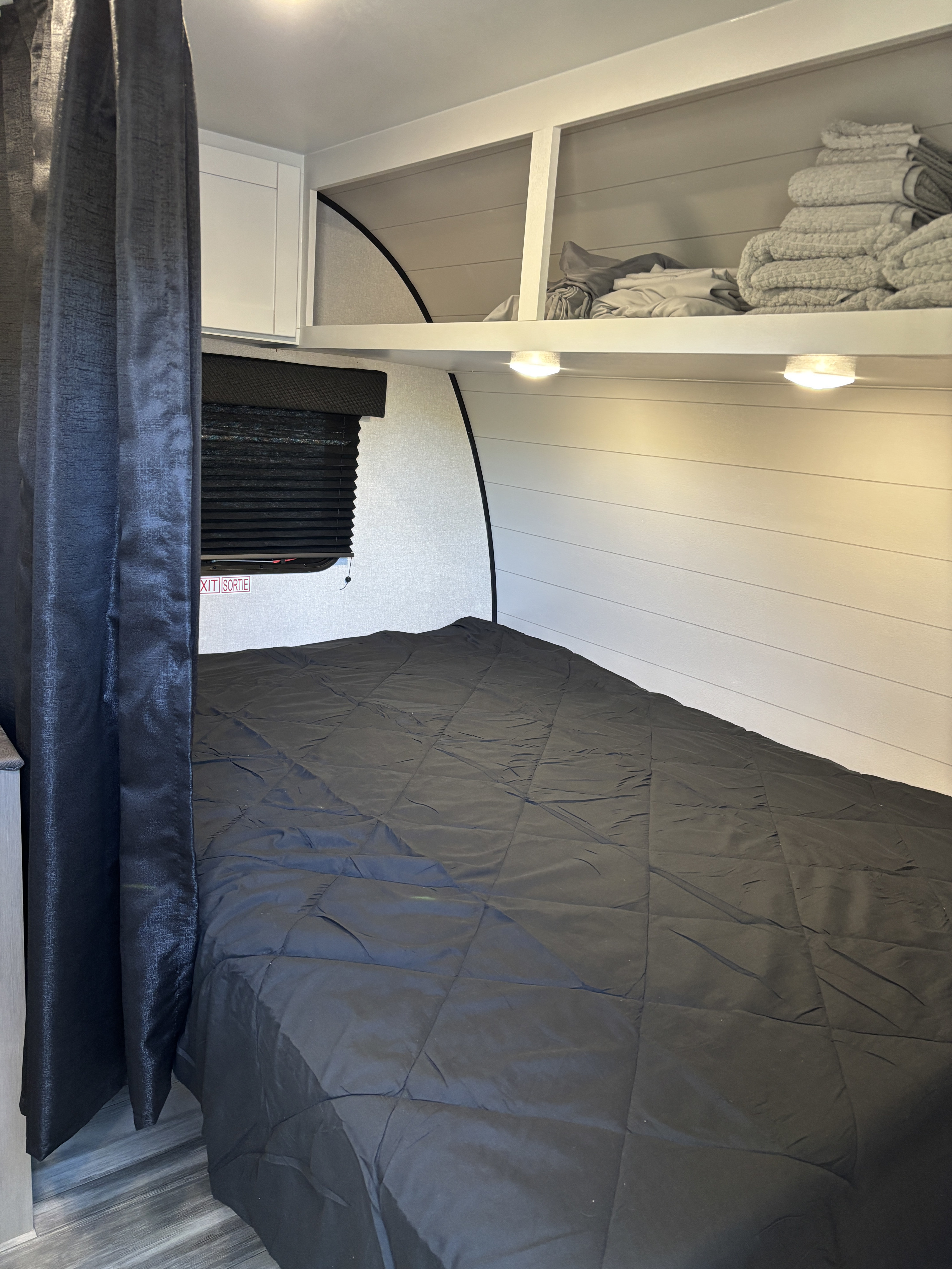 Cozy RV rental bedroom features a comfy black bed, overhead storage, and privacy curtains for your travels.. Jayco JayFlight 2026