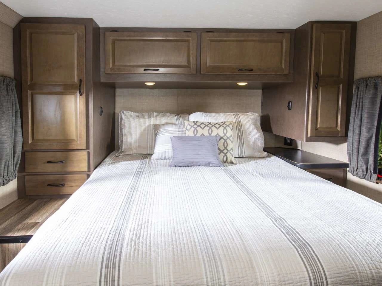 Cozy RV rental bedroom with striped bedding, overhead cabinets, and a wardrobe with drawers for storage and comfort.. Thor Majestic 2019