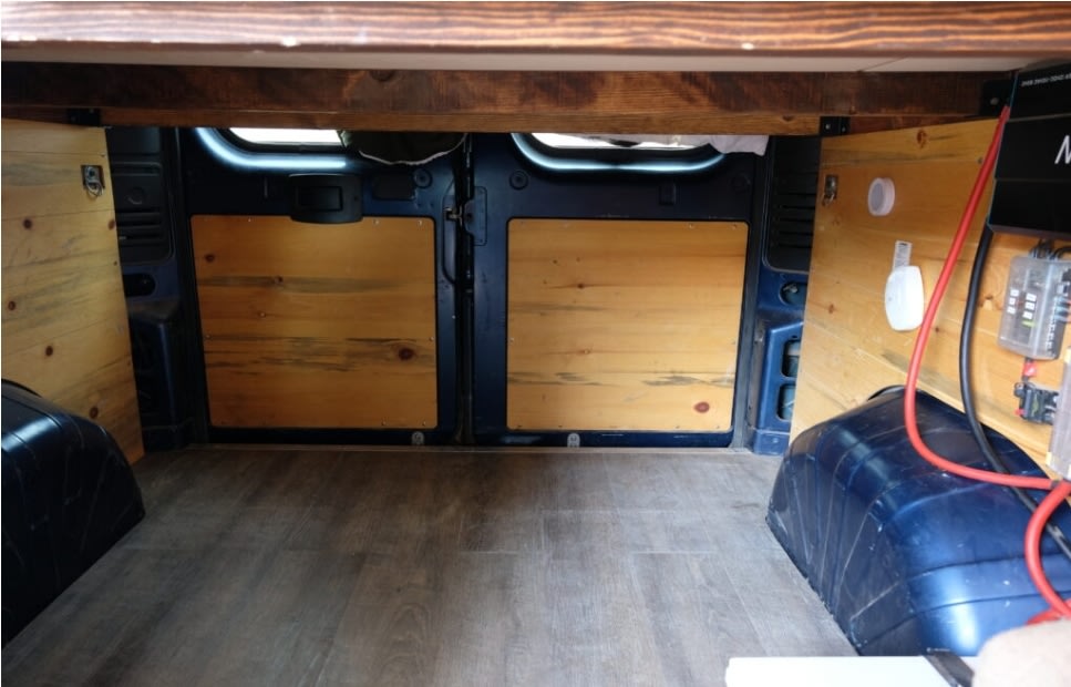 RV rental camper van interior, showing under-bed storage, wood paneling, electrical setup, and laminate flooring.. Dodge Ram 1500 2021