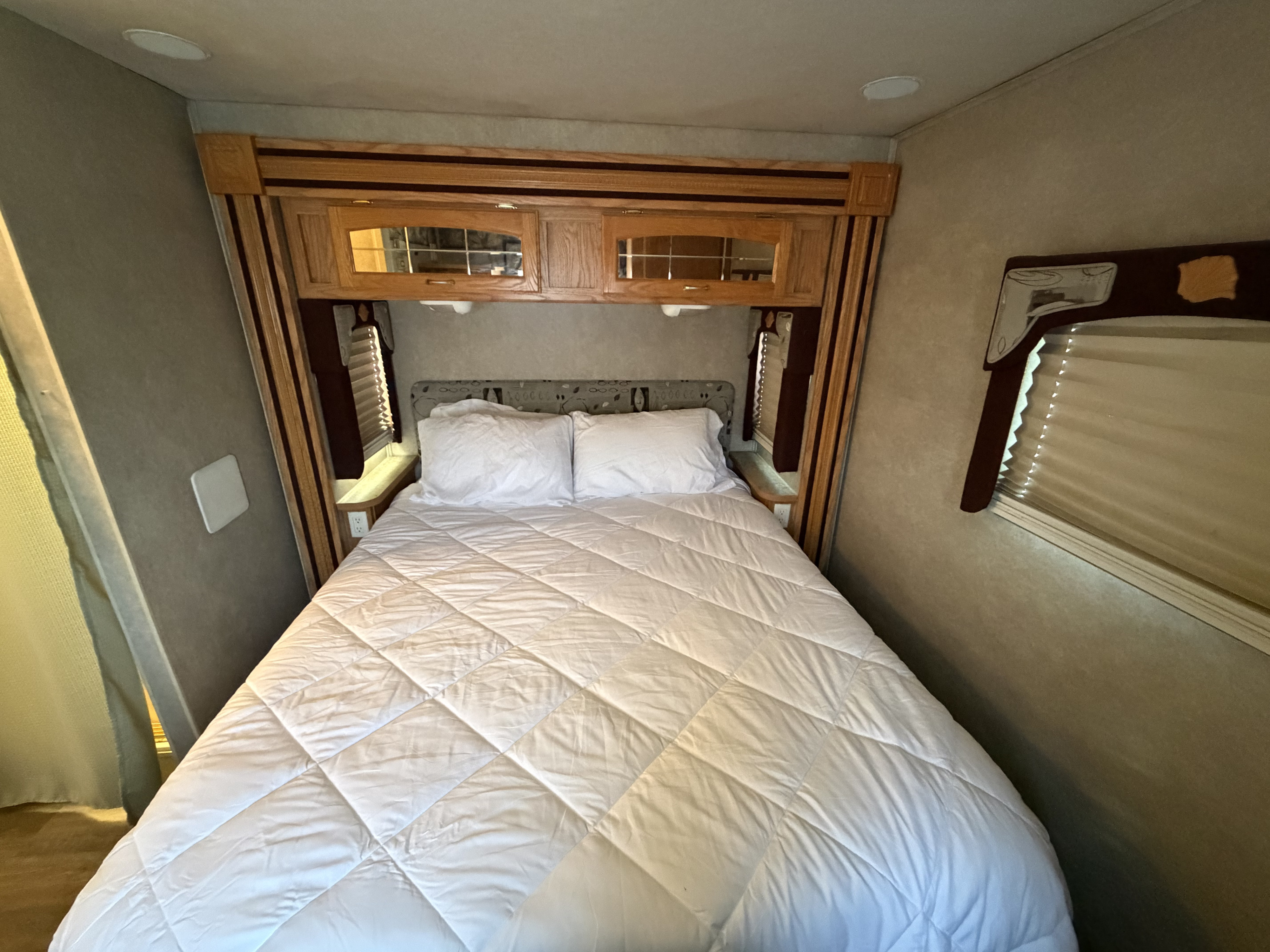 Cozy rv rental bedroom with a queen bed, white bedding, wood cabinets, and bedside outlet, perfect for a comfortable stay.. Jayco Greyhawk 2006