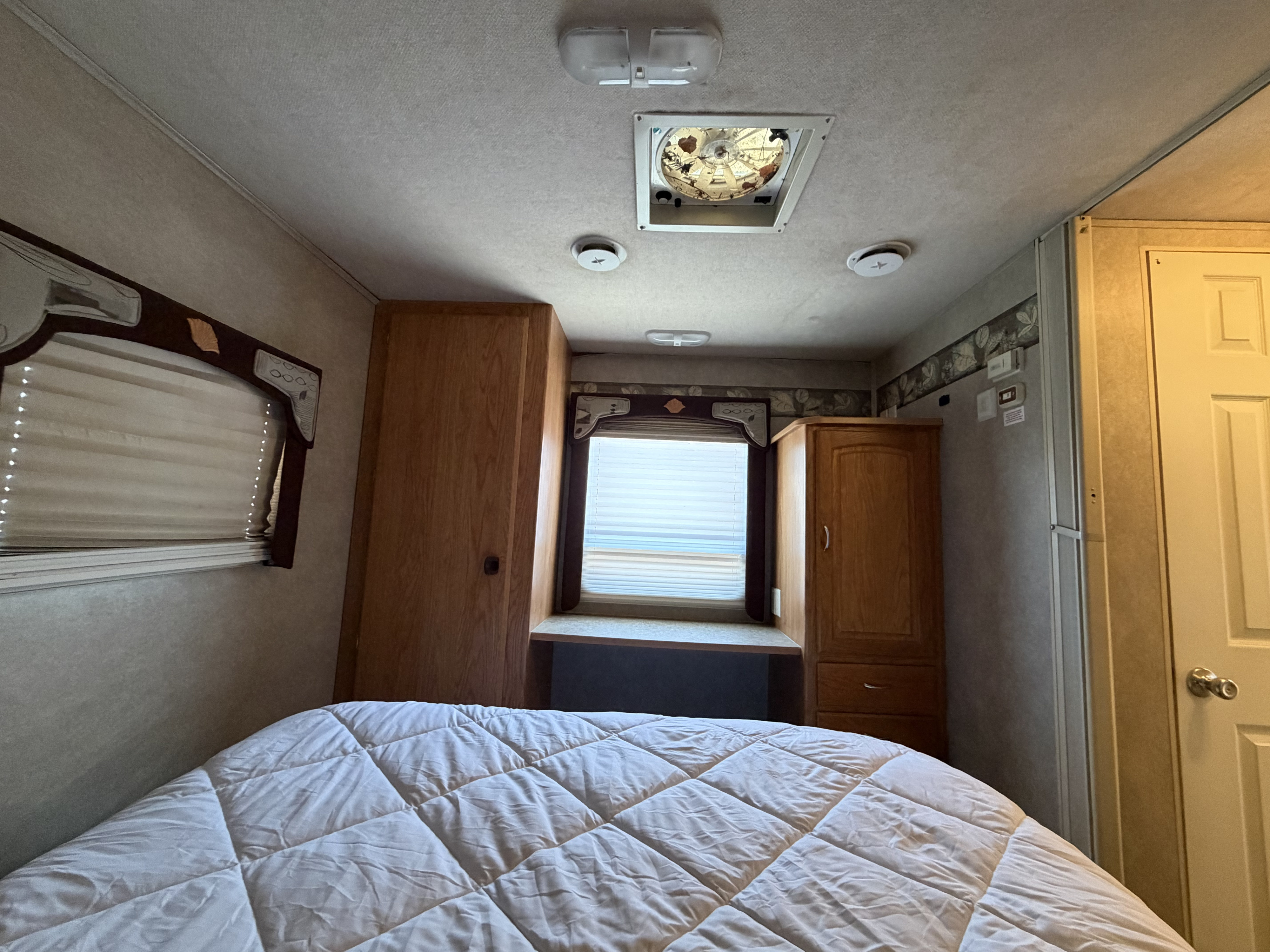 Explore this RV rental bedroom with a comfy bed, window, wood cabinets, and ceiling vent (some debris visible).. Jayco Greyhawk 2006