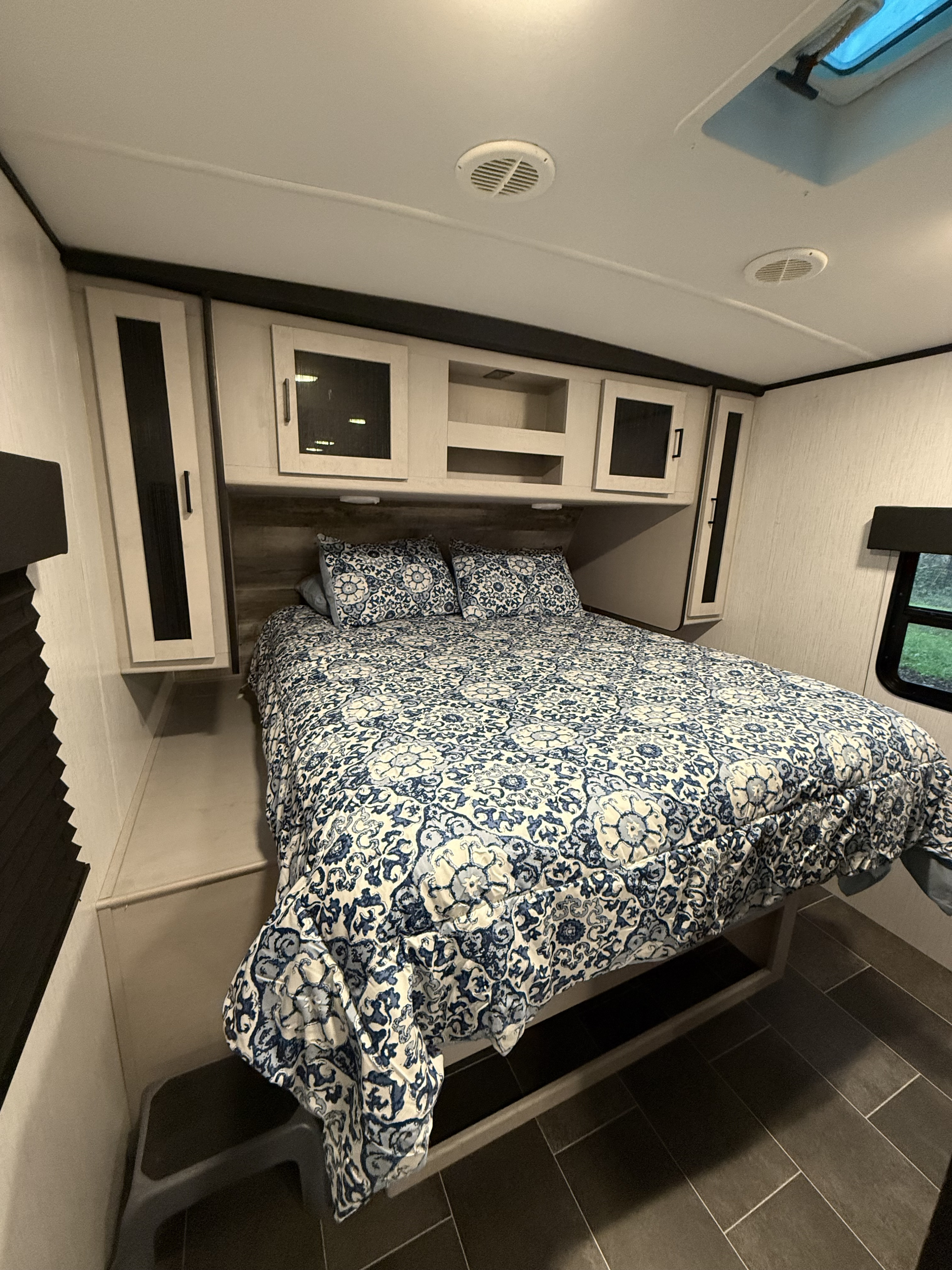 Comfortable RV rental bedroom featuring a bed with blue patterned bedding, overhead storage, and a side window.. Heartland RVs Mallard 2022