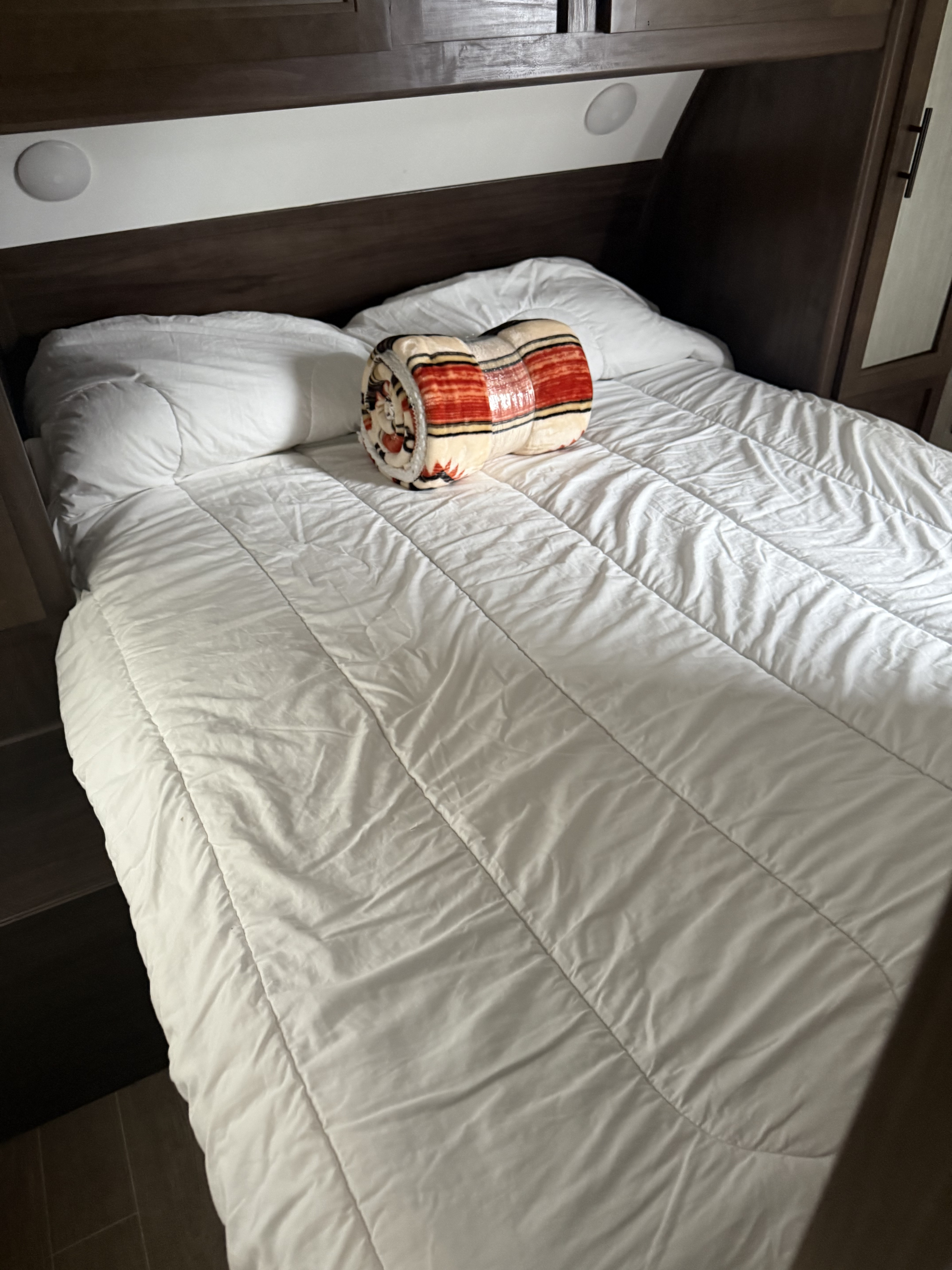 Cozy RV rental bedroom featuring a bed with white bedding, decorative blanket, and dark wood cabinetry with lights.. Forest River Cherokee Grey Wolf 2021