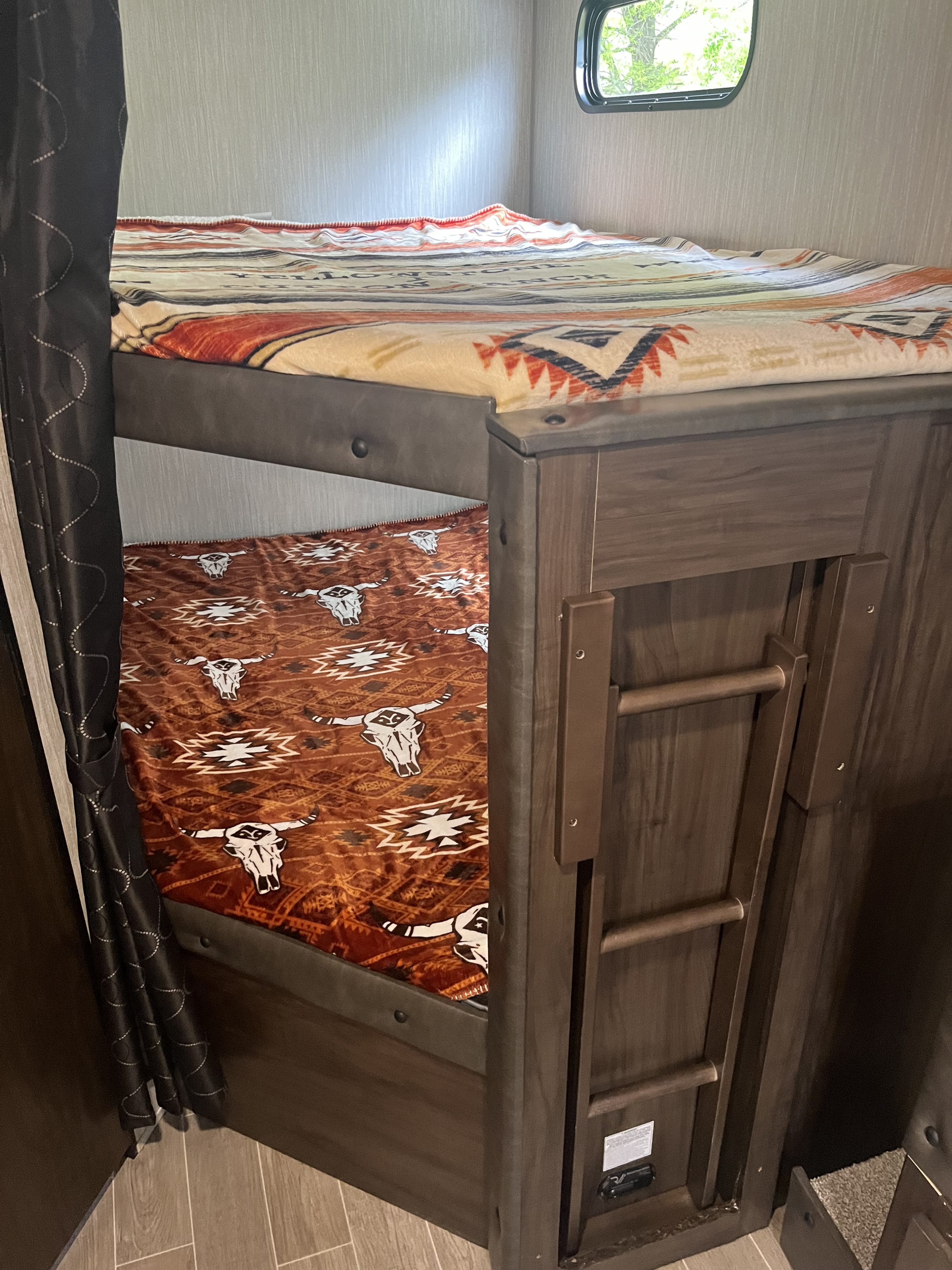 Cozy RV rental bunk beds with themed blankets, a ladder, and a window, offering comfortable sleeping accommodations.. Forest River Cherokee Grey Wolf 2021