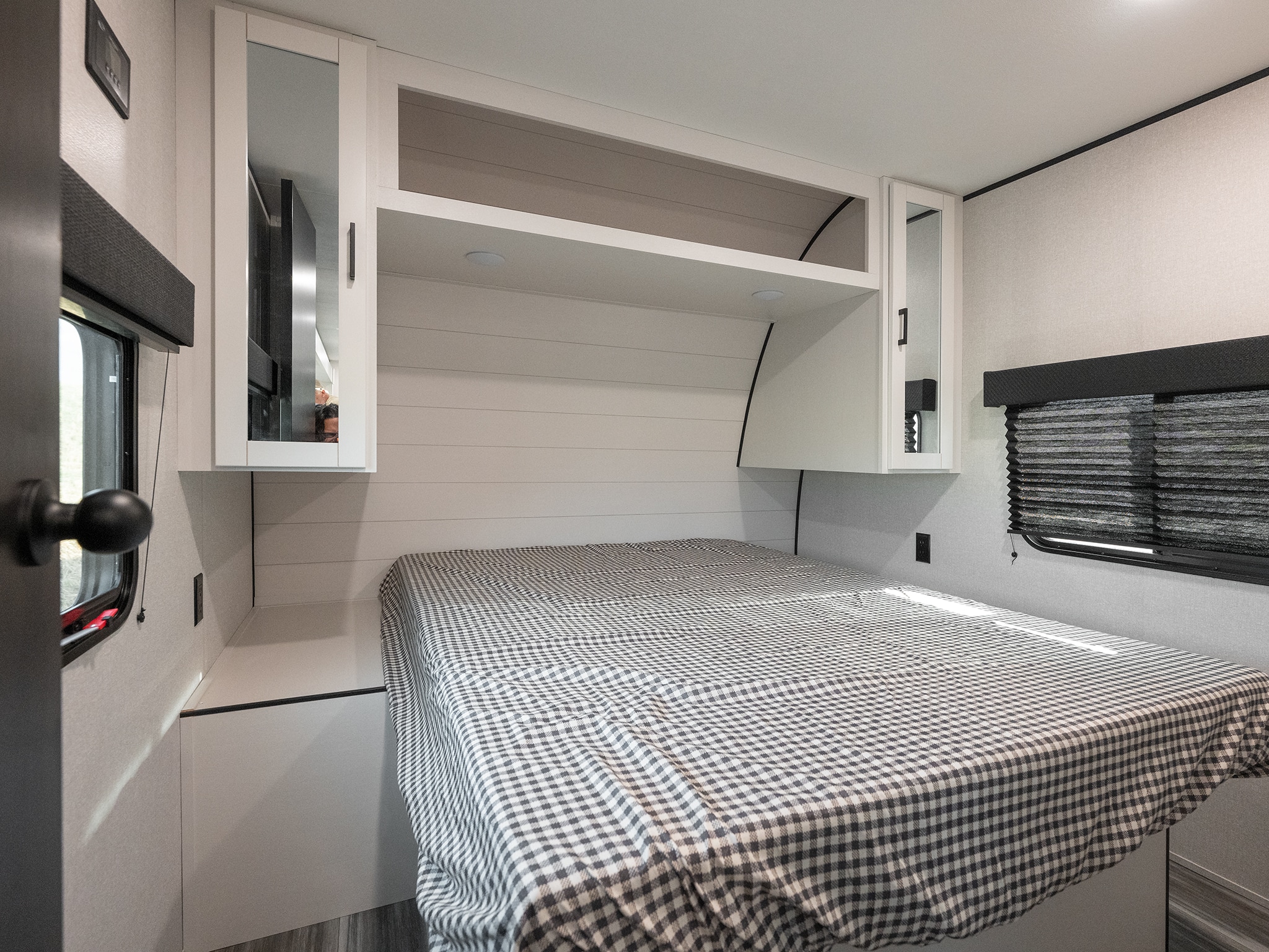 Comfortable RV rental bedroom featuring a bed with gingham bedding, overhead mirrored cabinets, and a built-in shelf.. Jayco Jay Flight 2026
